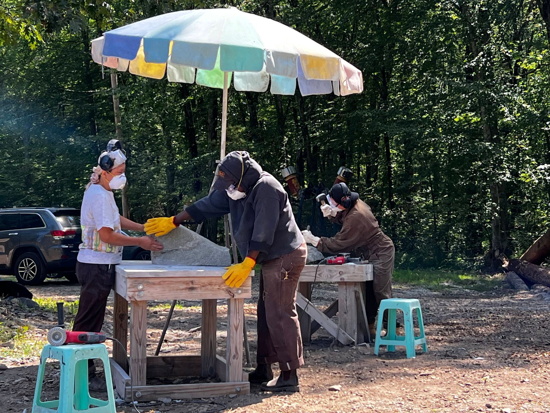 A whimsical metal sculpture in a grassy, wooded area. It features a yellow wheel, a clock face, and other repurposed elements.