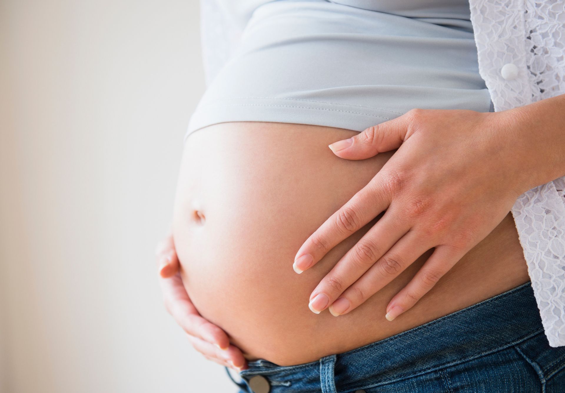 Pregnant person's hands gently cradling their belly, wearing jeans and a light blue shirt.