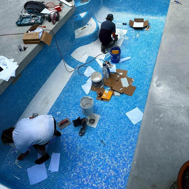 Two Men Are Working On A Swimming Pool With Blue Tiles — Byron Bay Luxury Pools in Evans Head, NSW