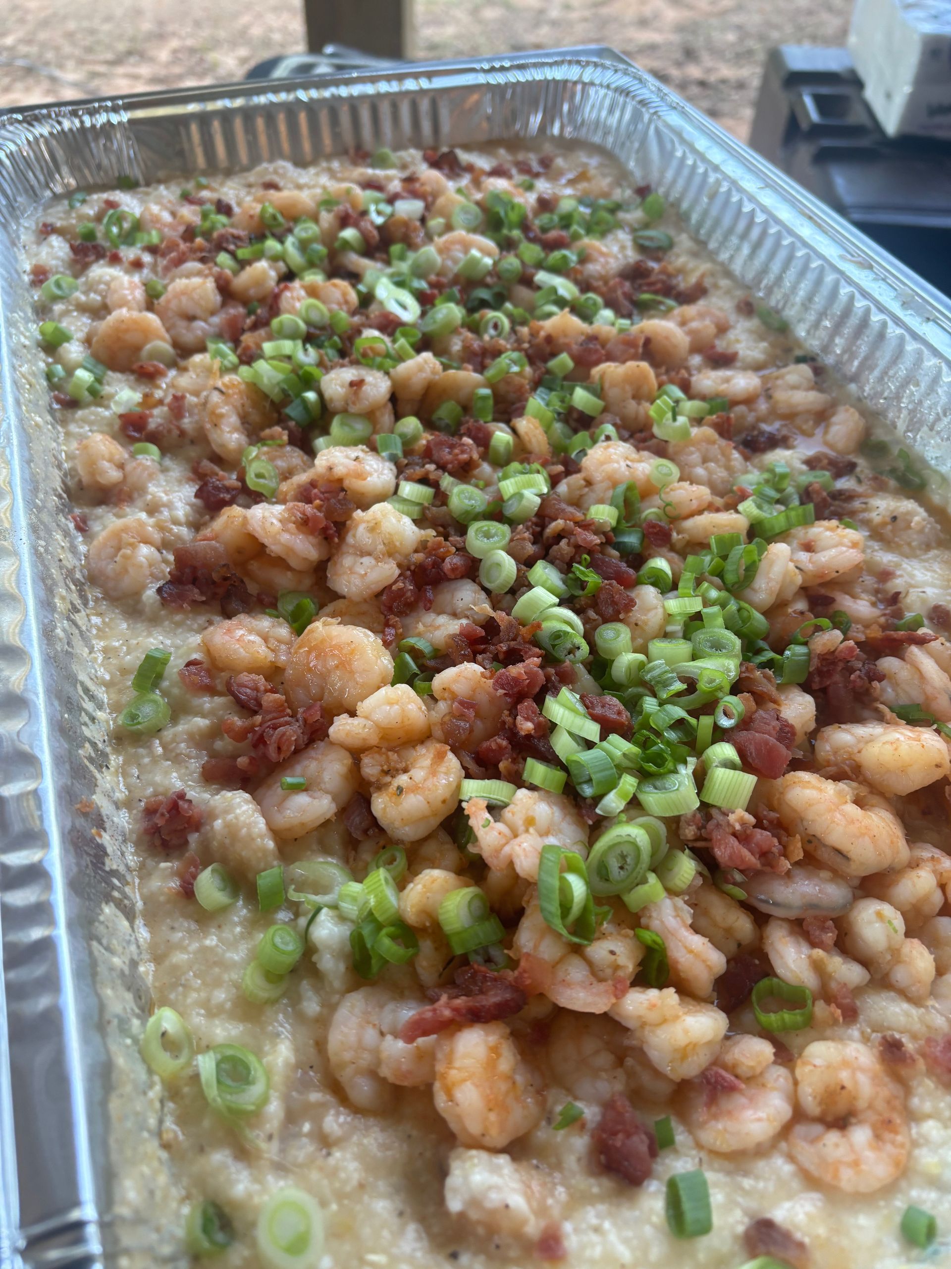 Tray of shrimp and grits topped with chopped green onions and bacon.