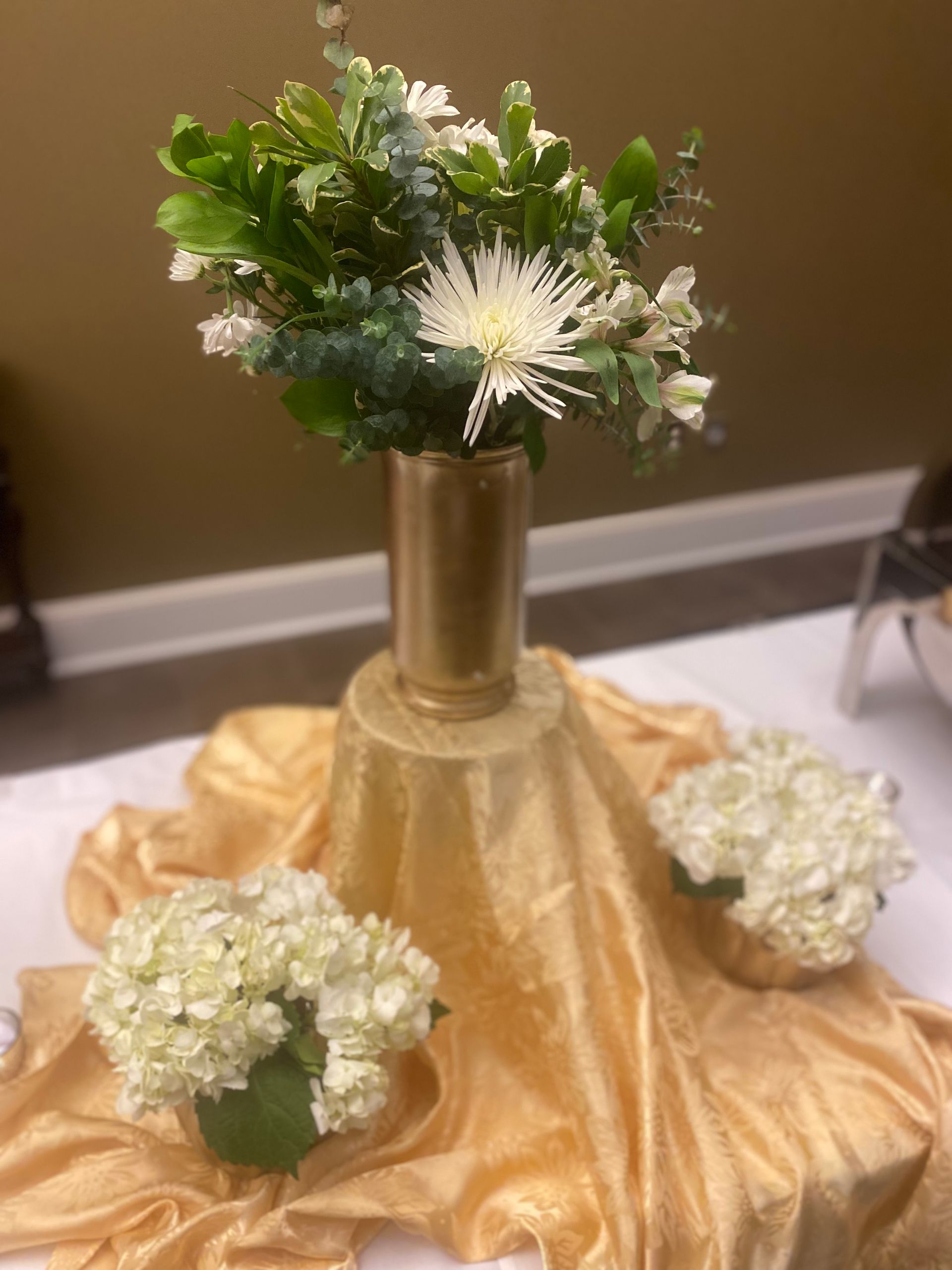 Golden table display with gold vase of flowers and white hydrangea arrangements.