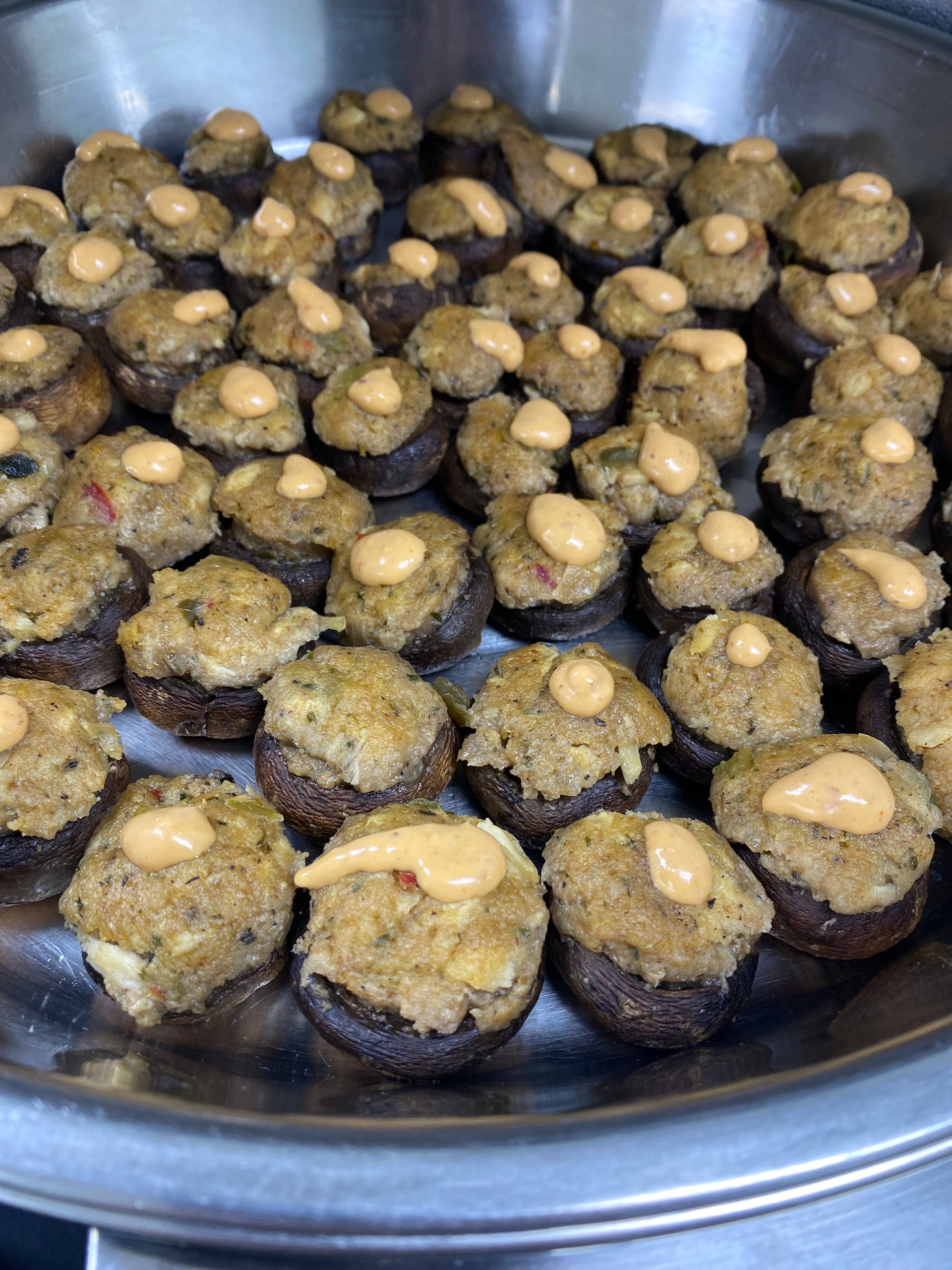 Stuffed mushroom appetizer in a metal tray. Brown mushrooms are filled with a savory stuffing and drizzled with orange sauce.