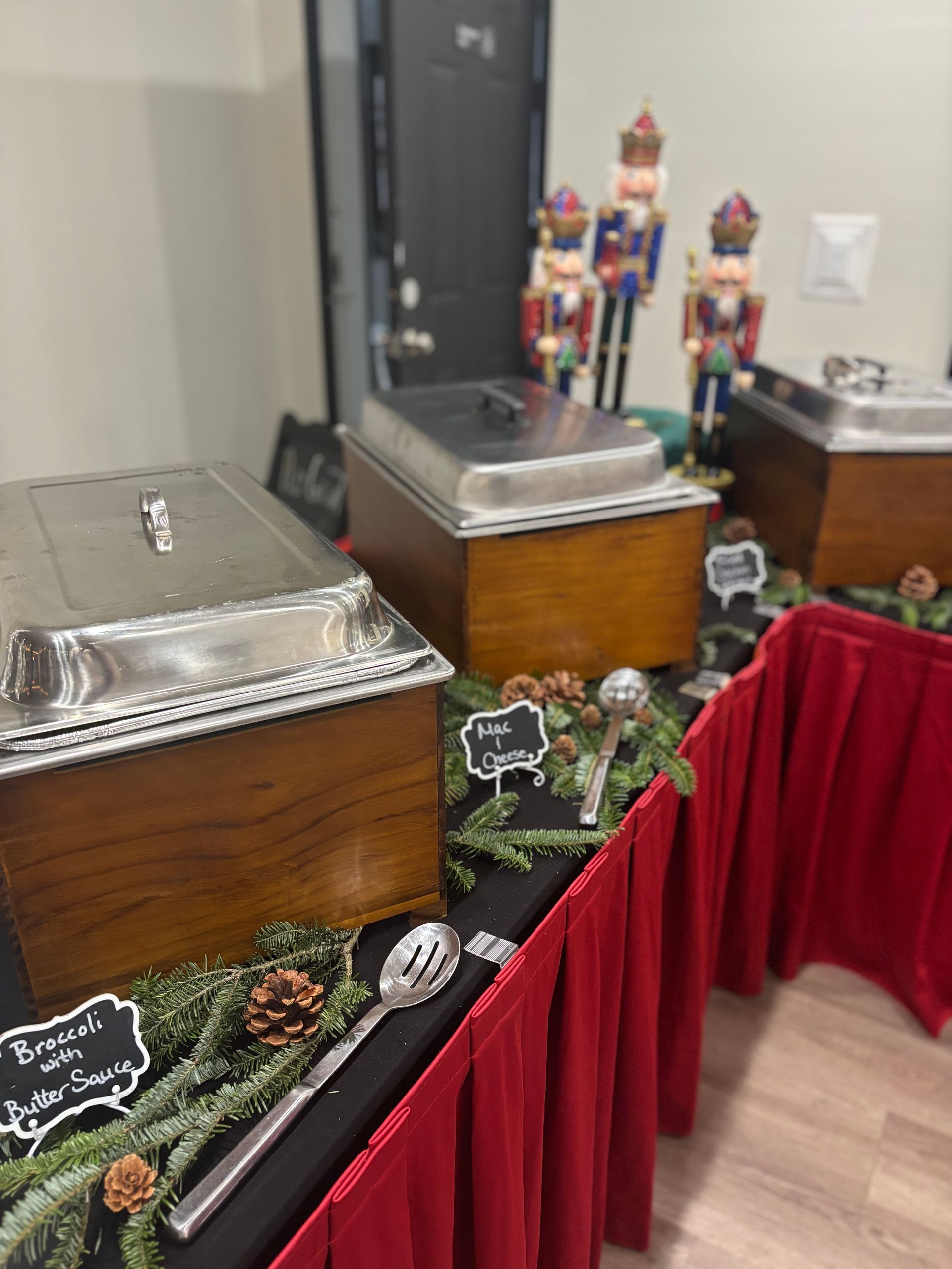 A buffet table with three food warmers, holiday decor, and red tablecloths. Nutcrackers stand in the background.