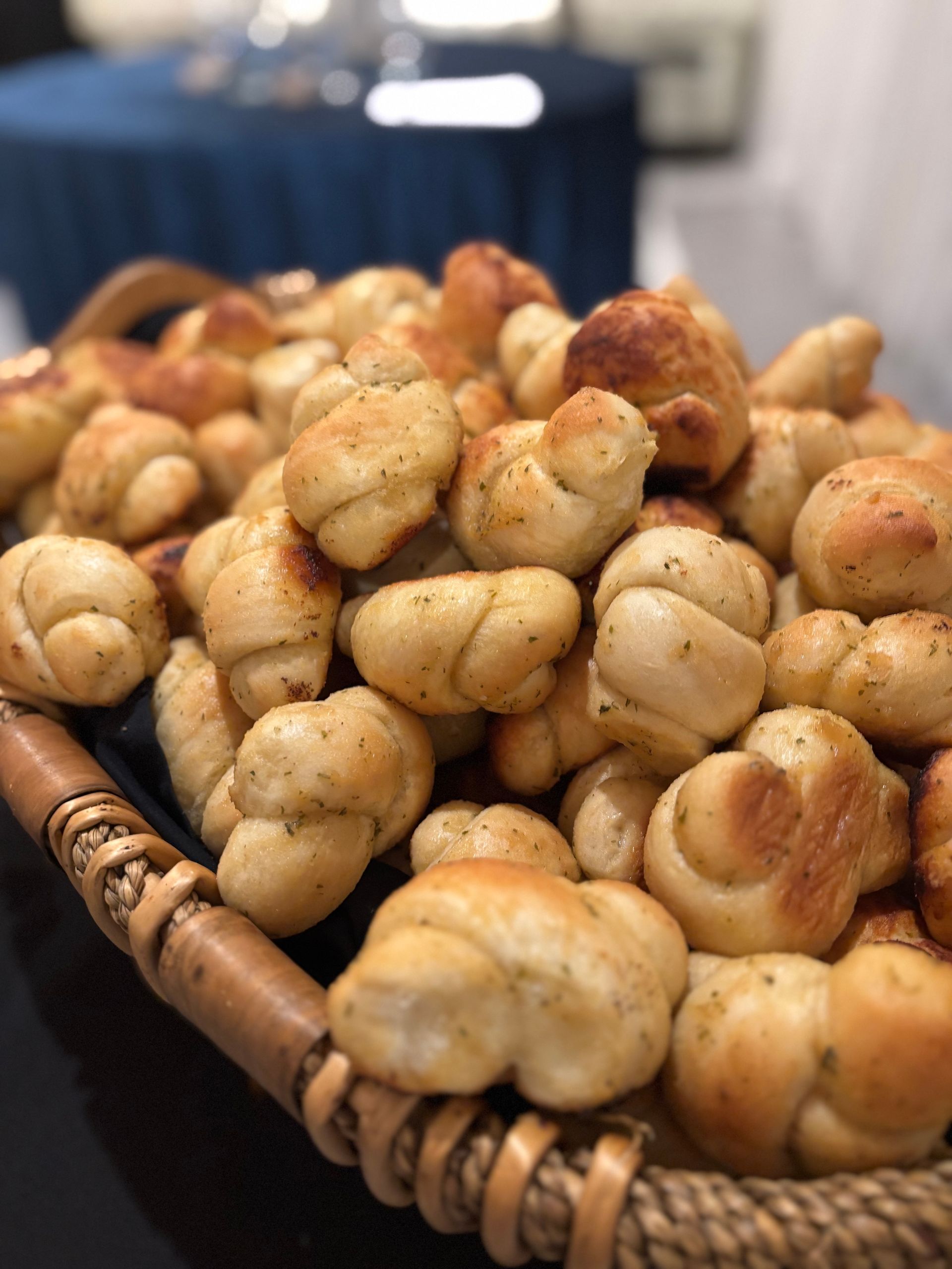 Basket overflowing with golden-brown garlic knots, a popular appetizer. Close-up view with a blurred background.