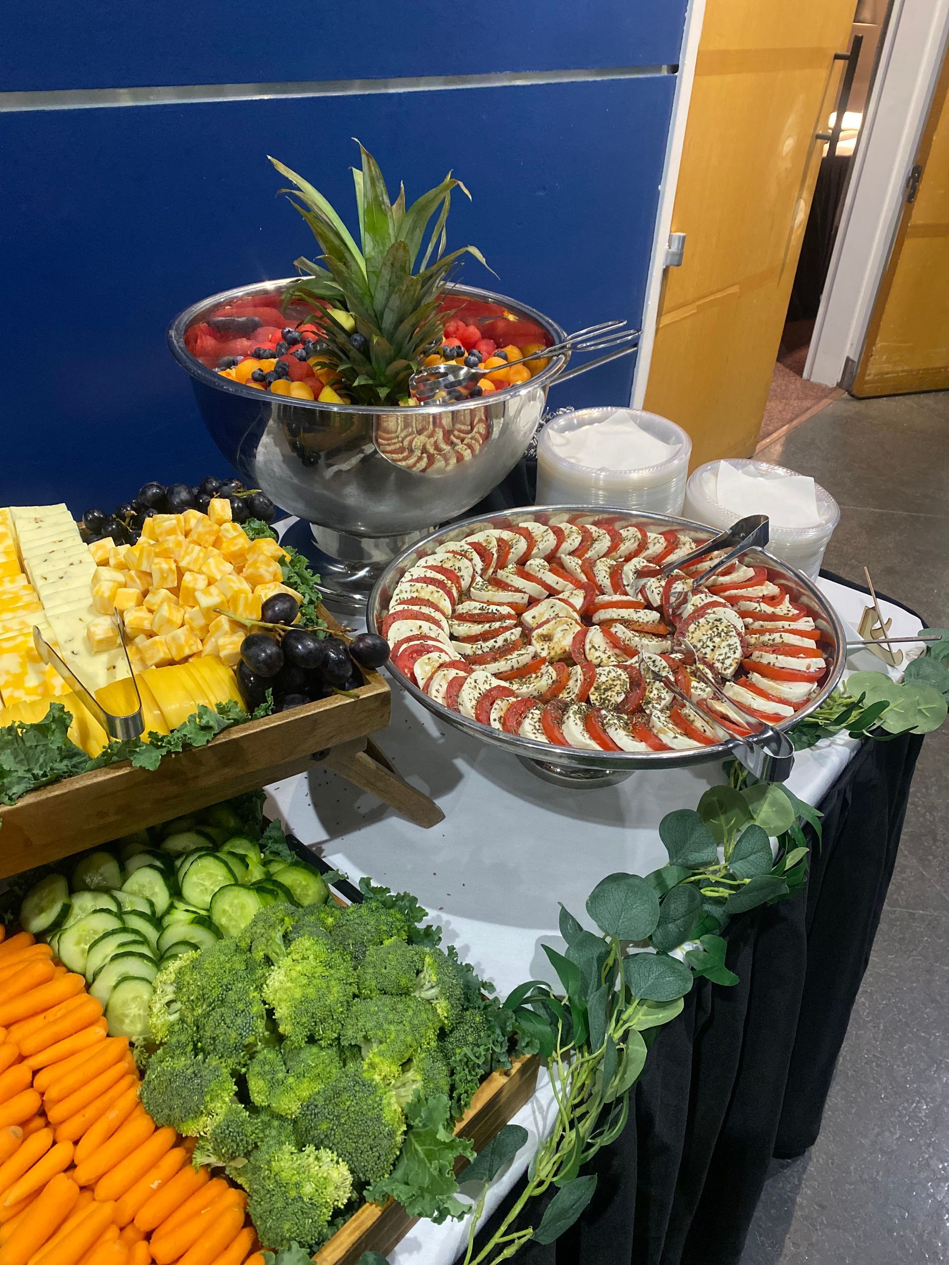 A buffet table with various food items: fruit, cheese, vegetables, and a tomato and mozzarella appetizer.