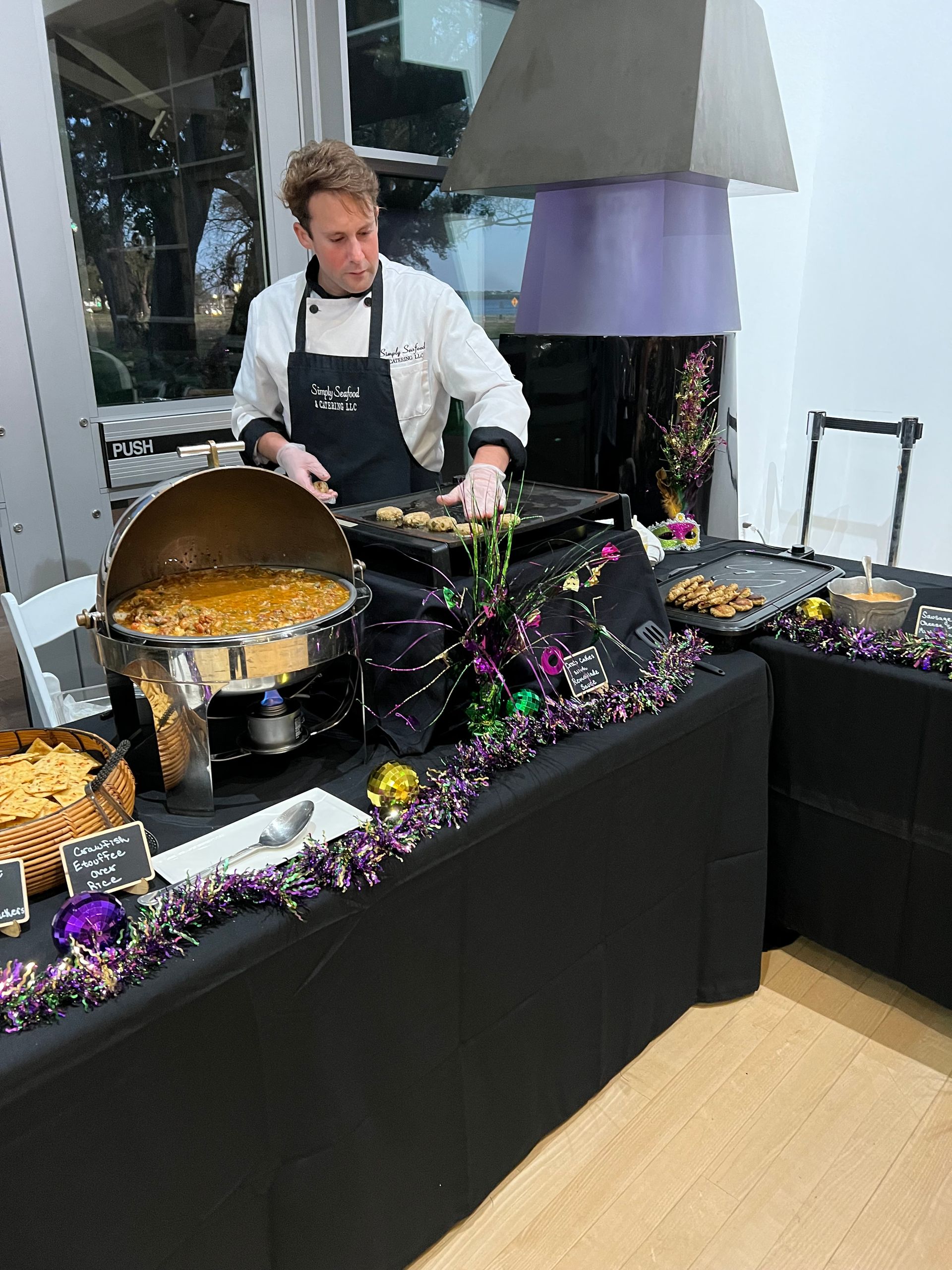Chef preparing food at a buffet. Black table decorated with Mardi Gras beads and a black tablecloth.