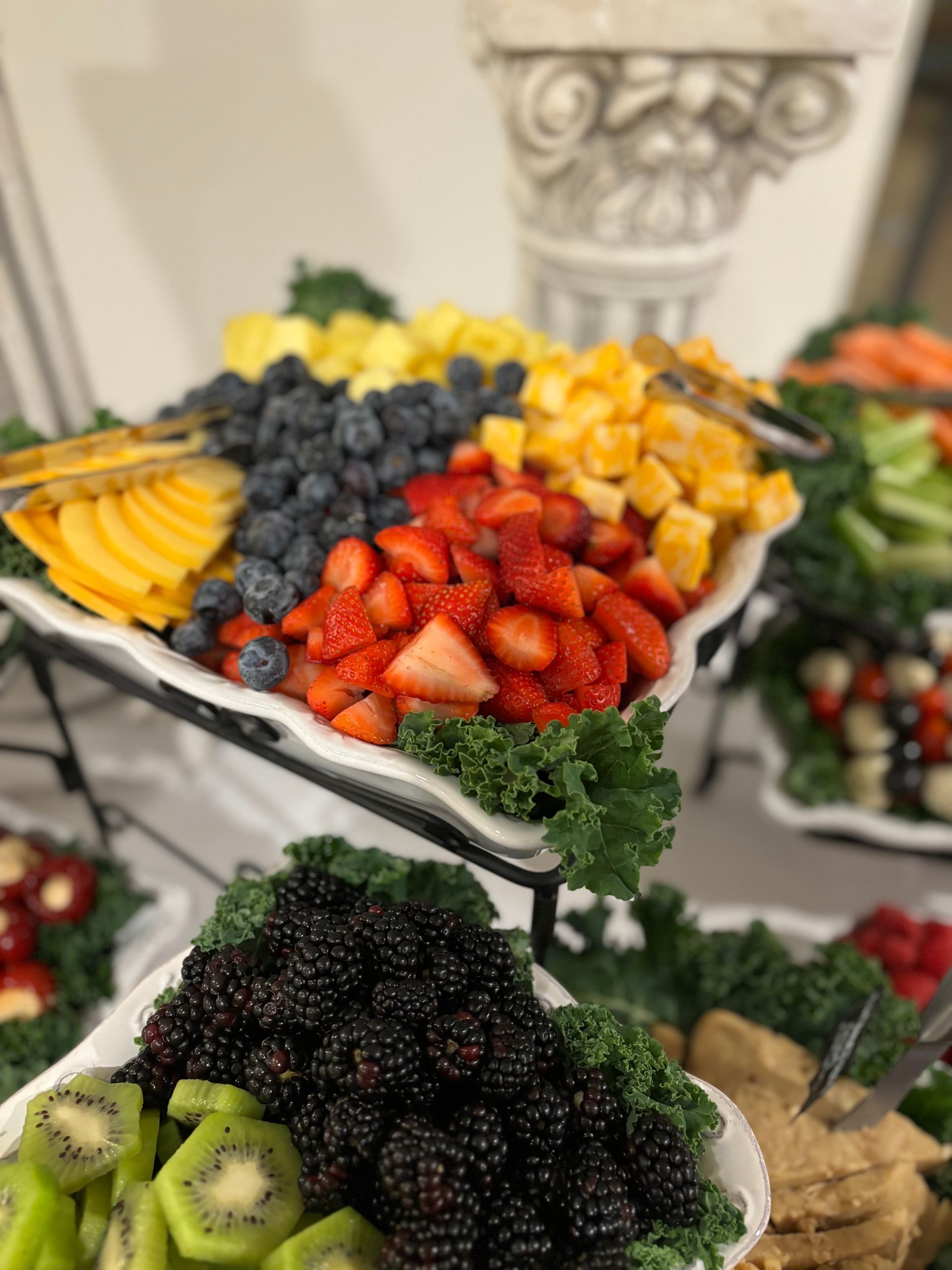 Fruit platter with strawberries, blueberries, pineapple, kiwi, and blackberries. Presented on a tiered display with garnishes.