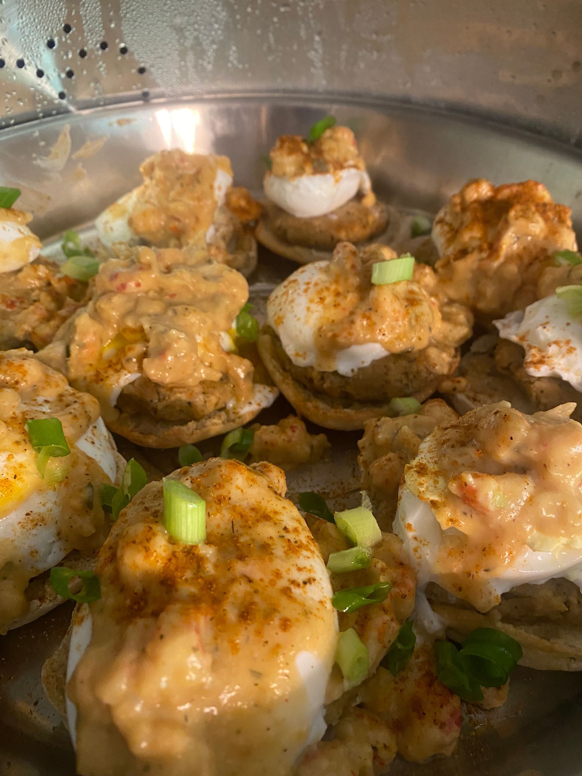 Deviled eggs topped with a creamy sauce and sprinkled with paprika and green onions, served on a metal surface.