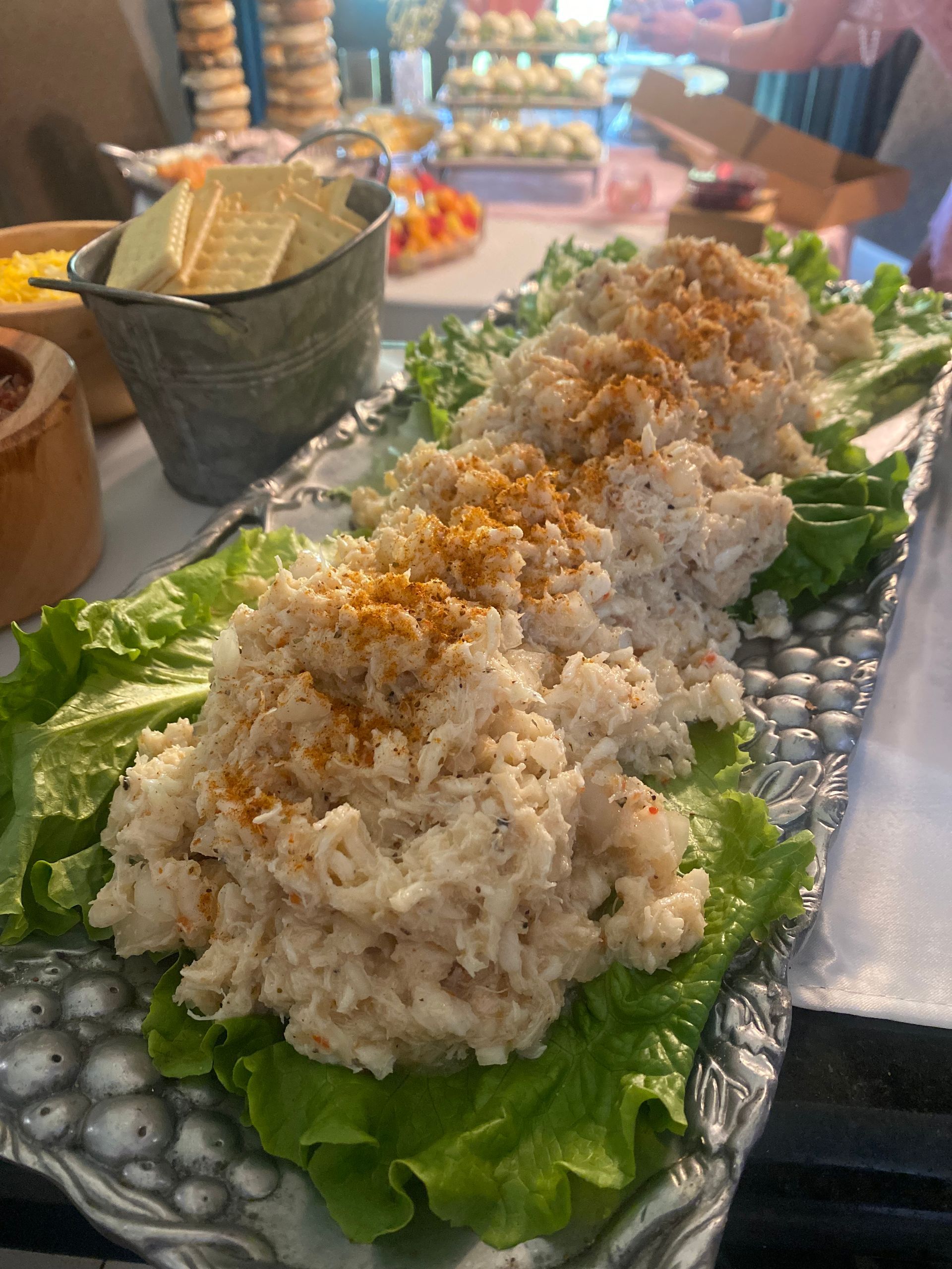 A platter of white crab salad on a bed of green lettuce, garnished with a sprinkle of orange powder, on a buffet table.
