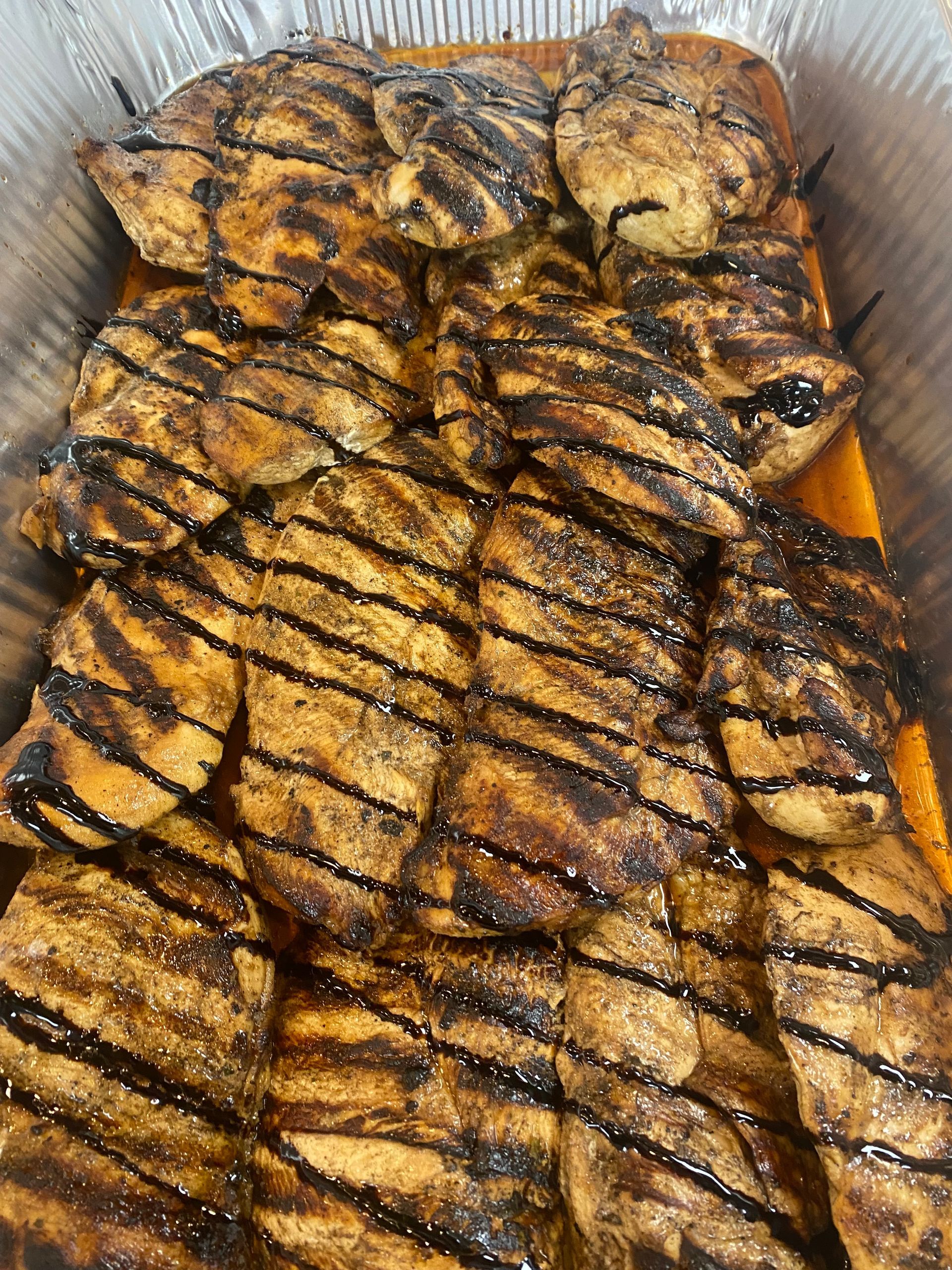 Grilled chicken breasts in a foil pan, showing dark grill marks.