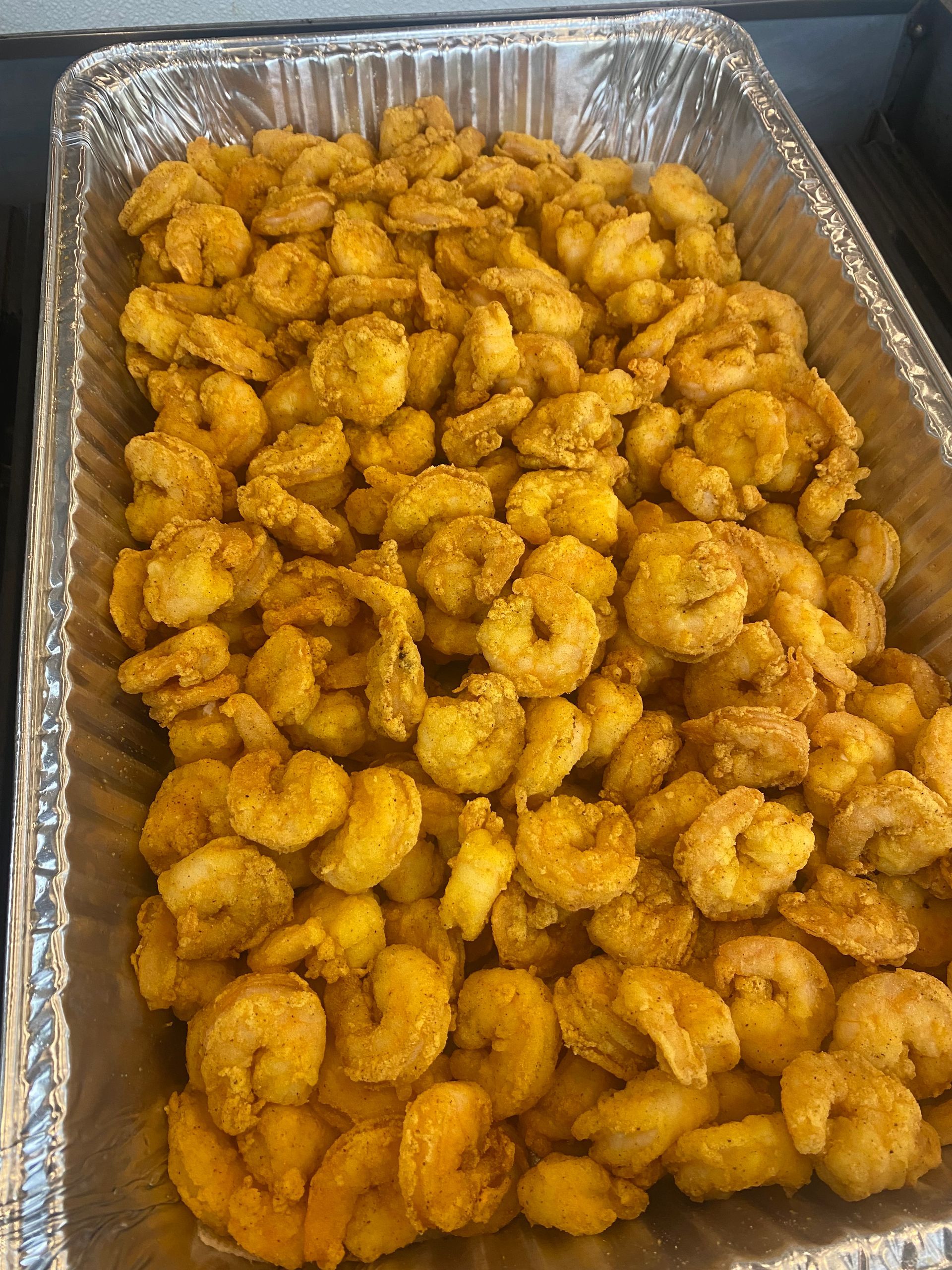 A tray of fried shrimp, golden brown, is ready to be served. They are in a silver tray.