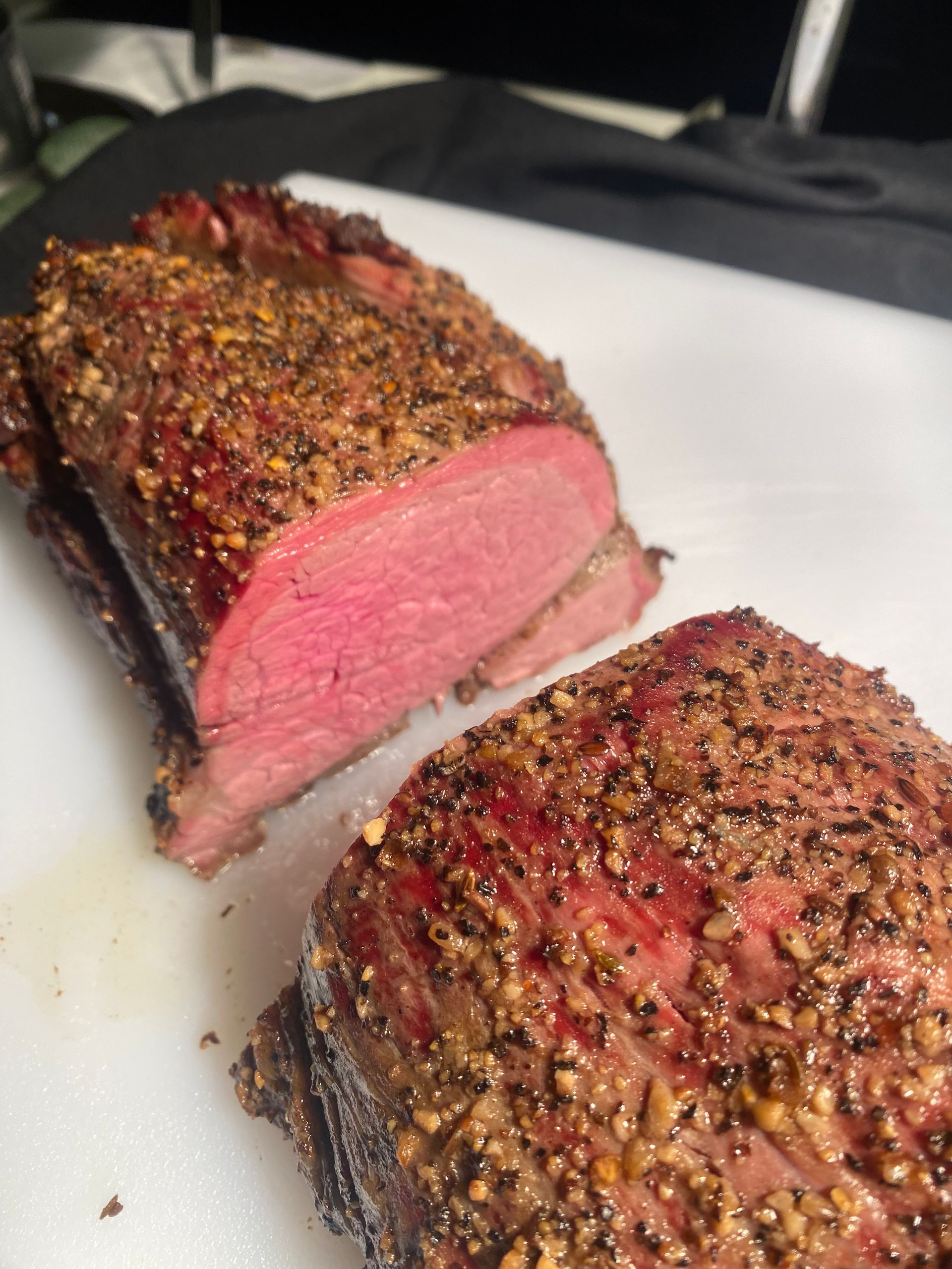 Sliced roast beef, medium-rare, on a white cutting board. The meat is reddish-pink with a seasoned crust.