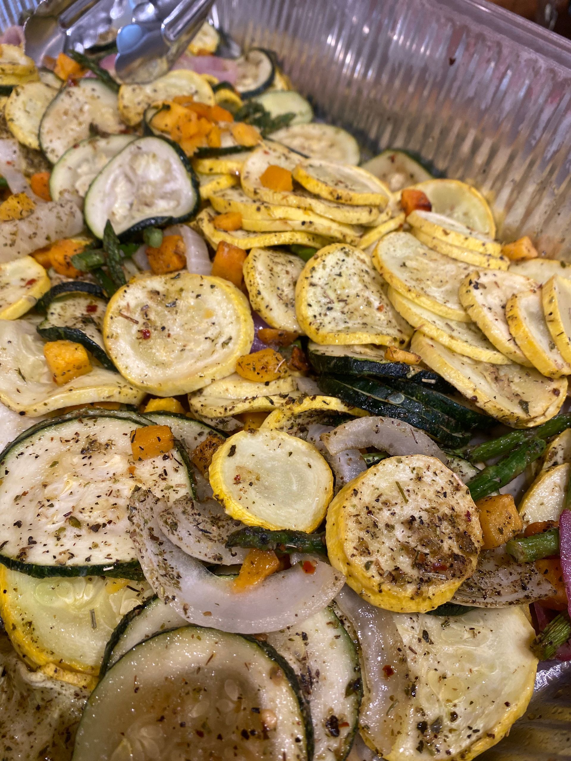 Roasted vegetables in a tray, including zucchini, yellow squash, onion, and butternut squash, seasoned with herbs and pepper.