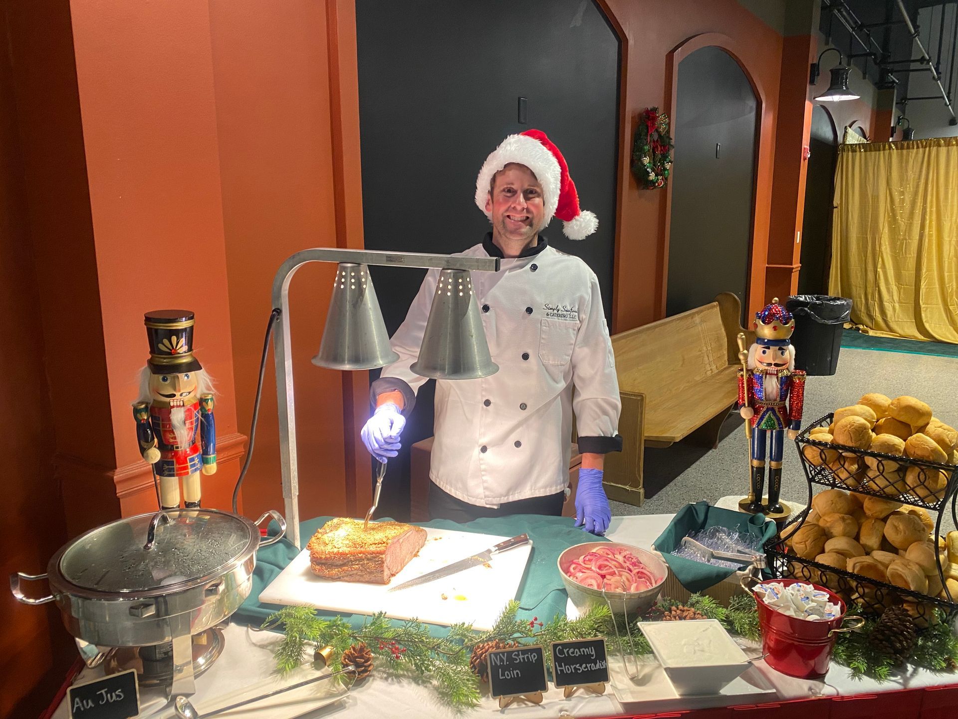 A chef wearing a Santa hat carves meat at a buffet table decorated for the holidays.