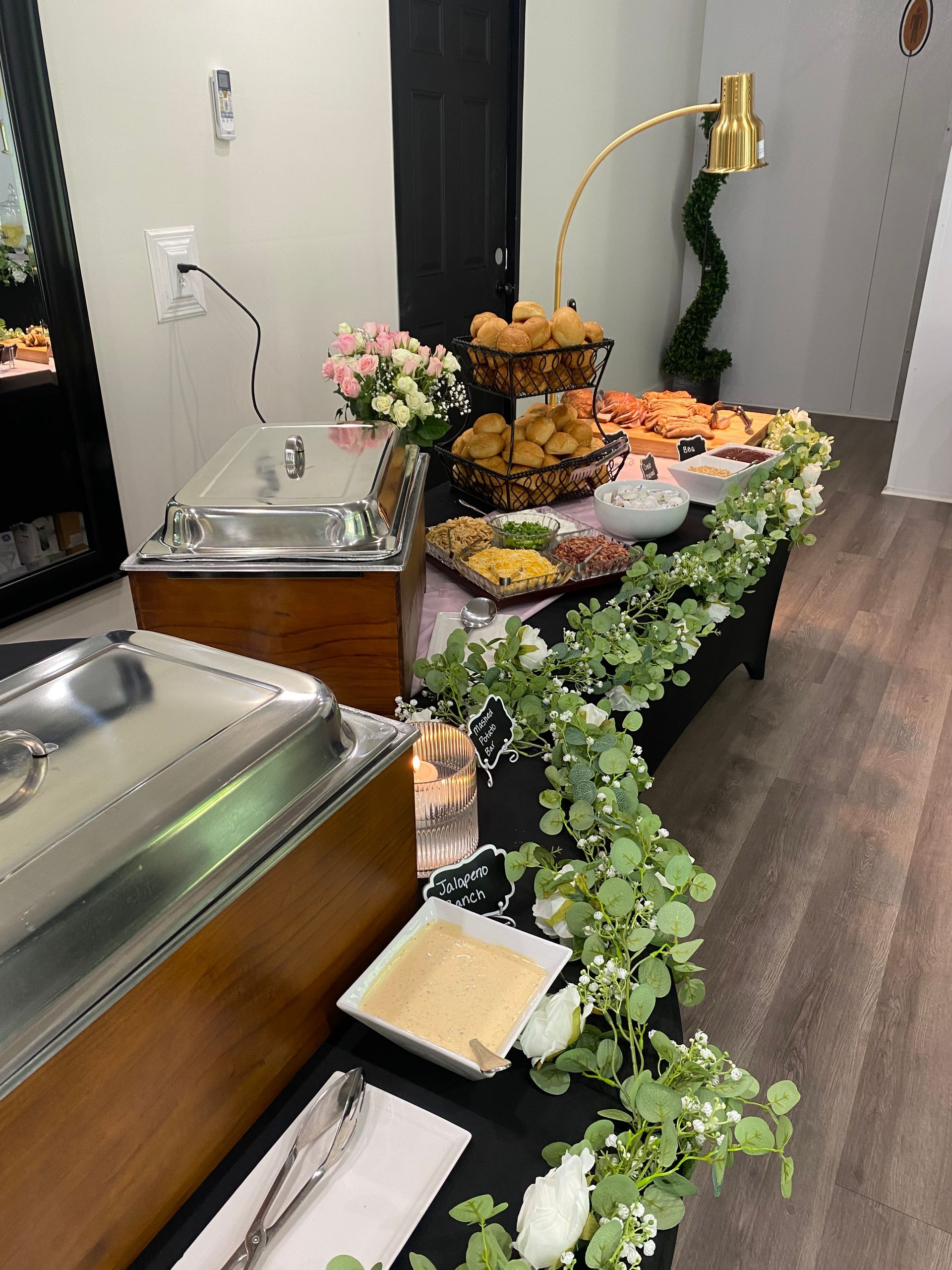 A buffet table with various food items, decorated with flowers and greenery, set up indoors.  Two chafing dishes are in the foreground.