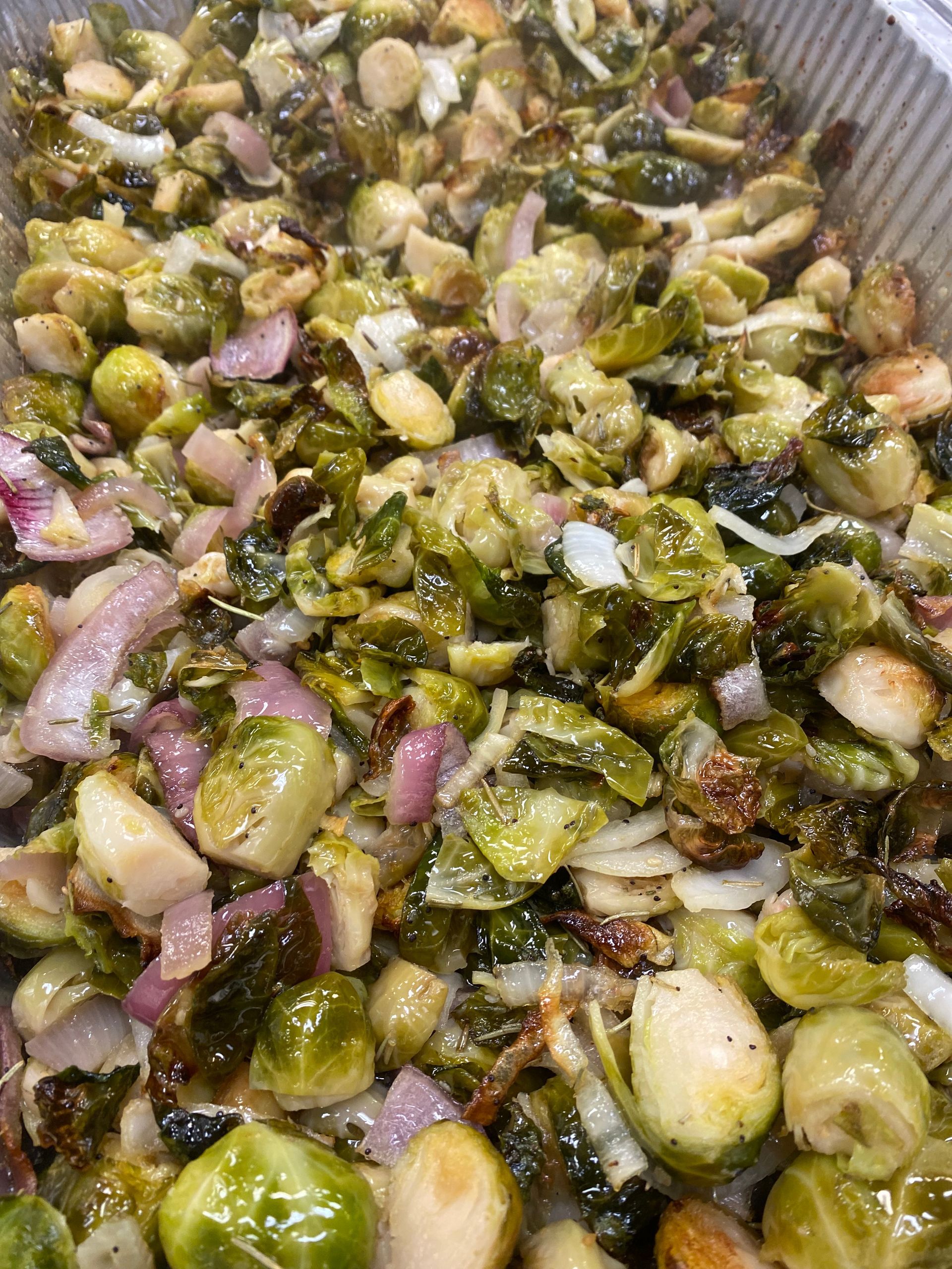 Roasted Brussels sprouts, red onion, and garlic in a metal pan; a mix of greens, browns, and purples.