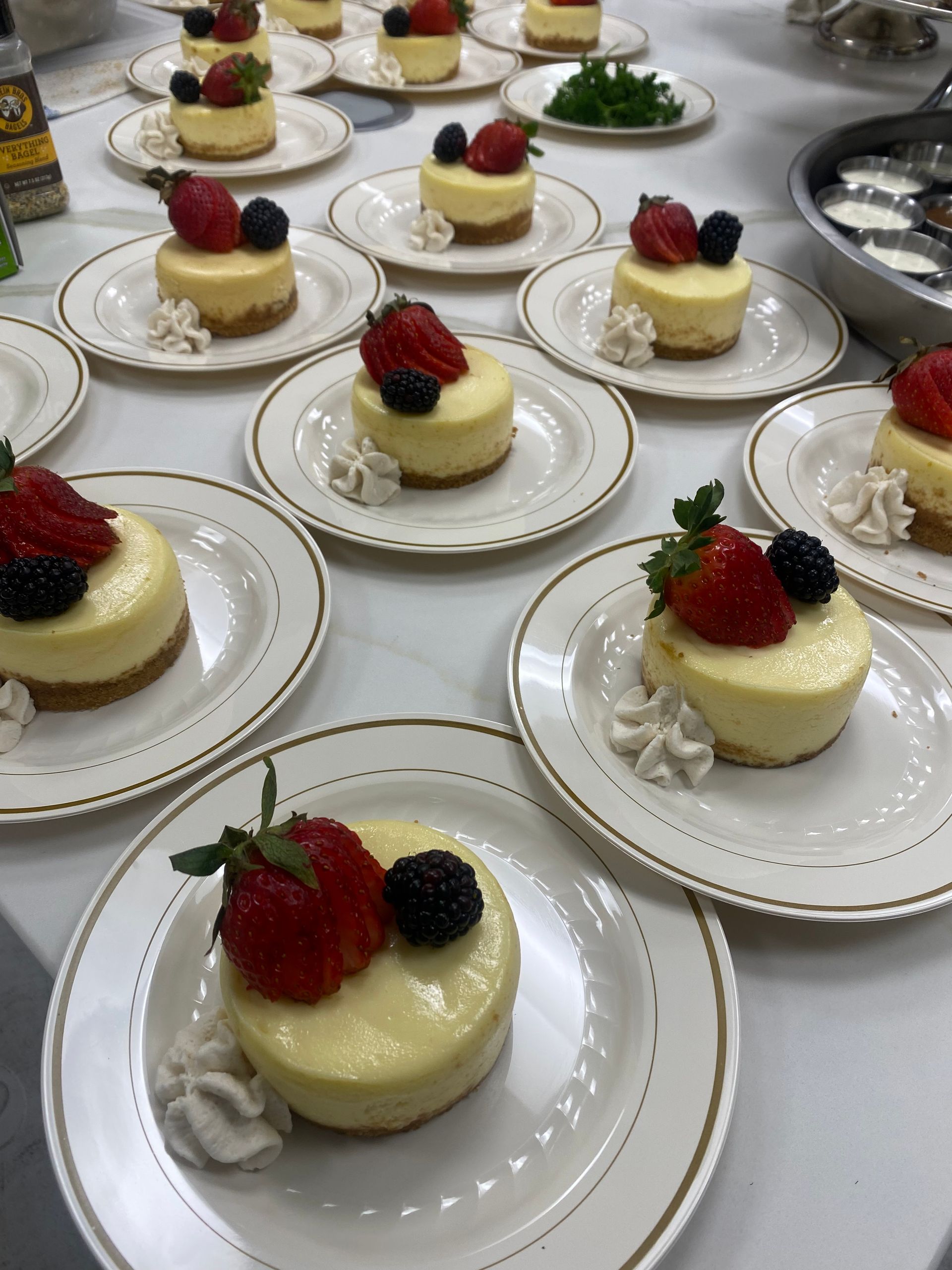 Mini cheesecakes topped with strawberries and blackberries, served on white plates with gold rims, arranged on a table.
