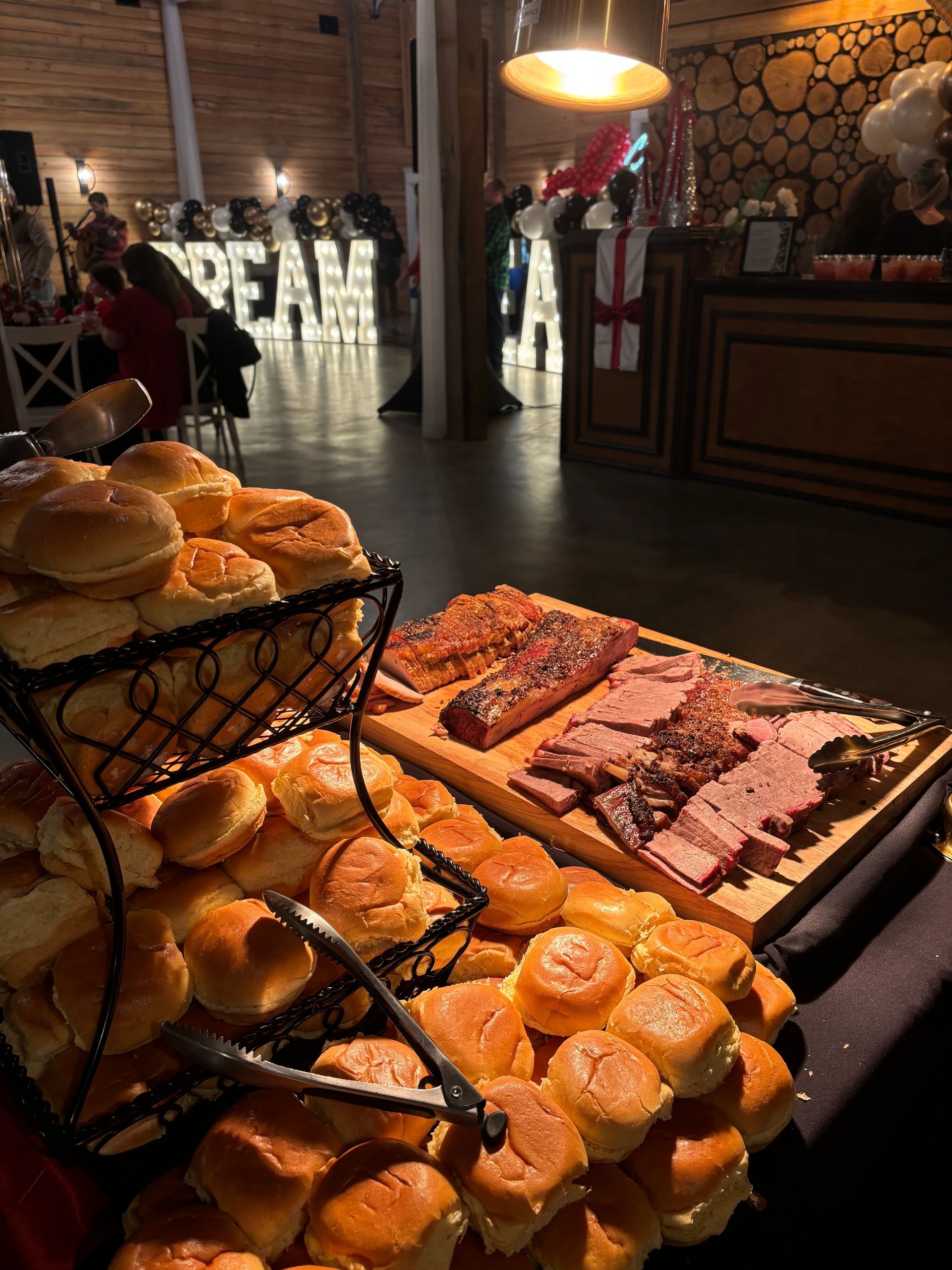 Buffet table with bread rolls and sliced meats, lit by an overhead light at a formal event. 