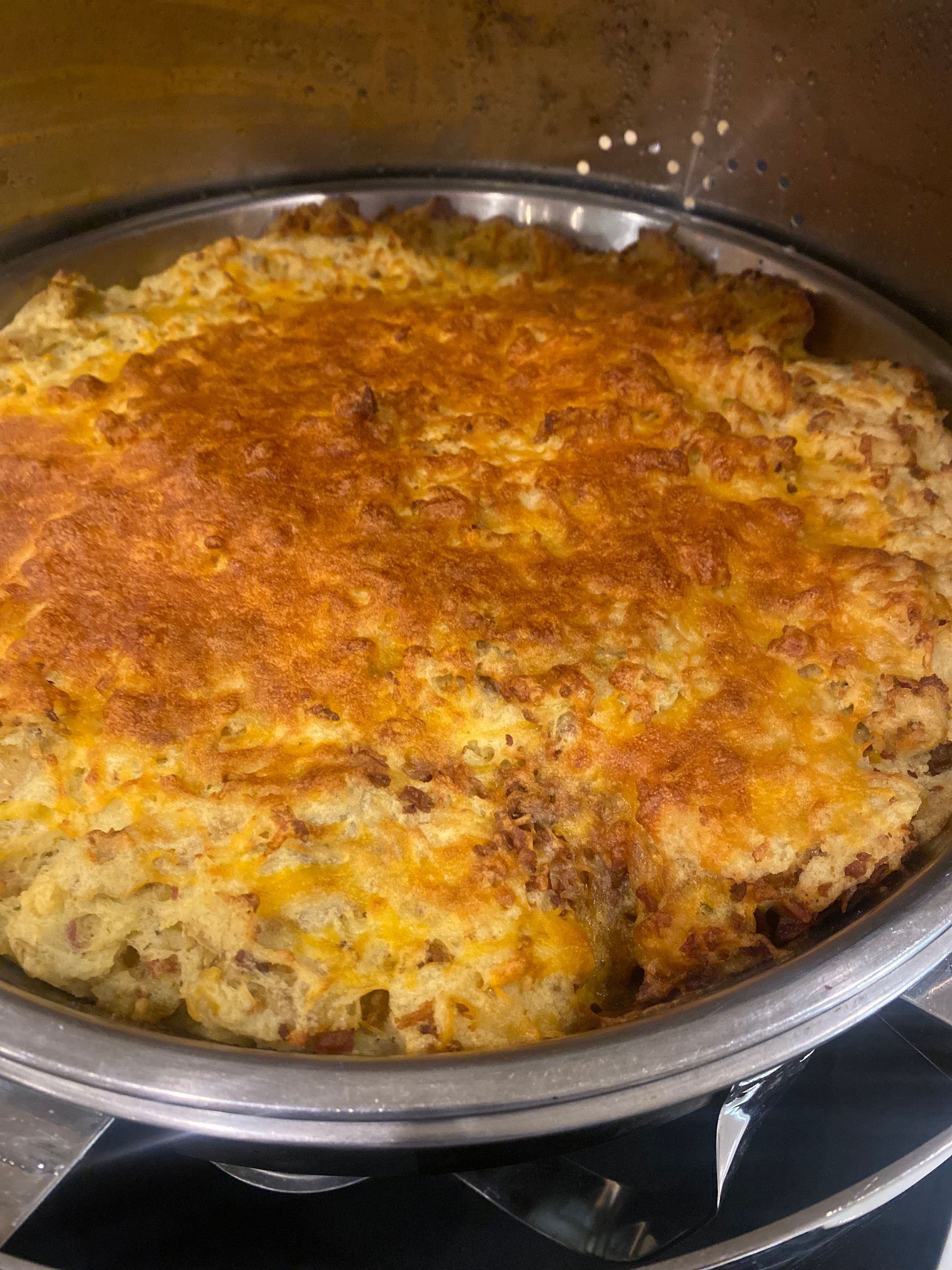 A golden-brown casserole in a silver dish. The food appears to be baked and bubbling.