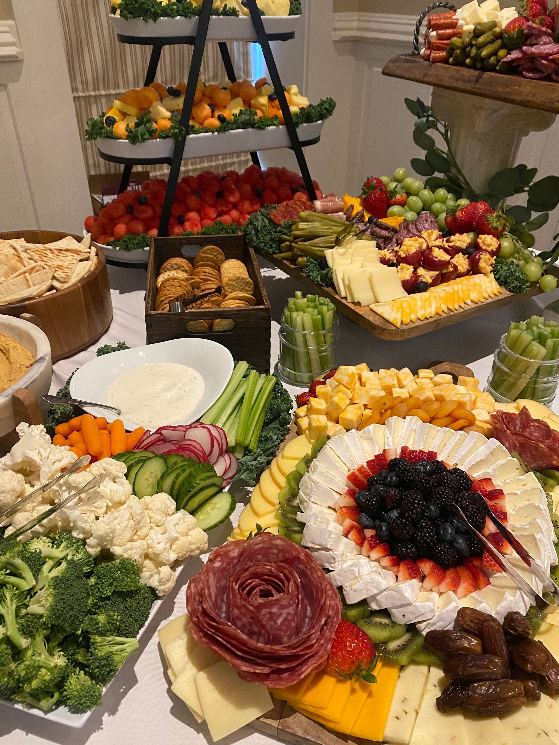 A lavish party spread of cheeses, fruits, vegetables, meats, and dips arranged on multiple levels.