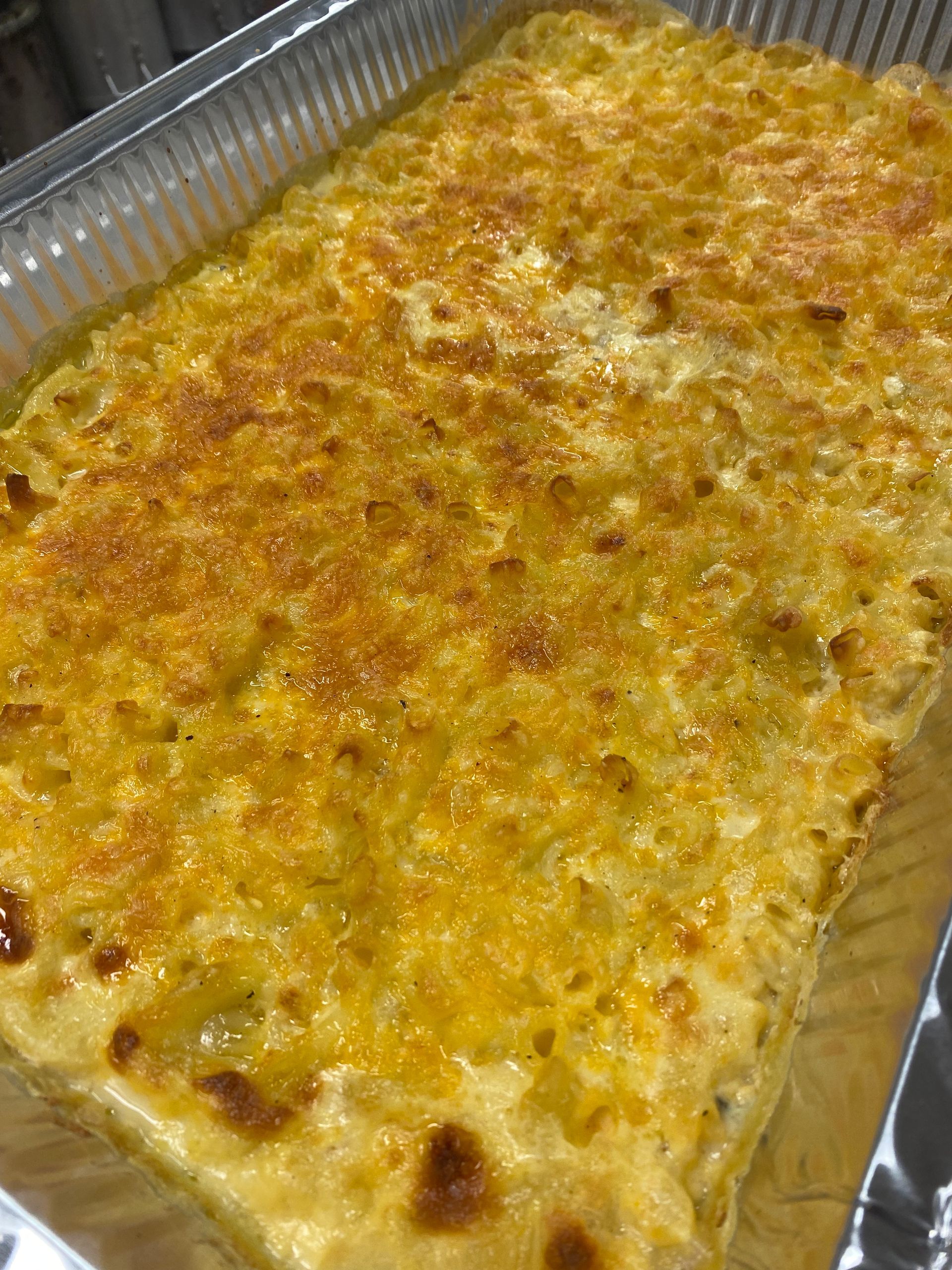 Macaroni and cheese casserole in a rectangular aluminum pan, golden brown and bubbly on top.