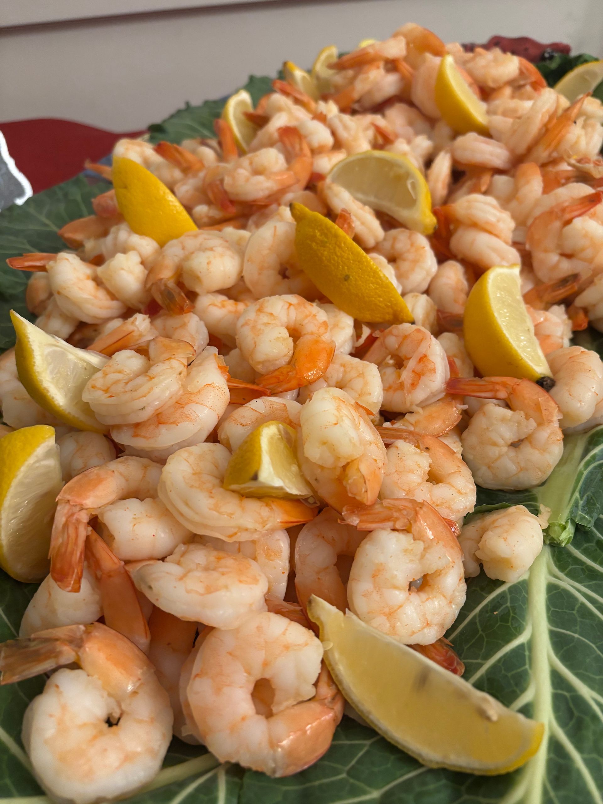 Cooked shrimp piled on a green leaf, garnished with lemon wedges.