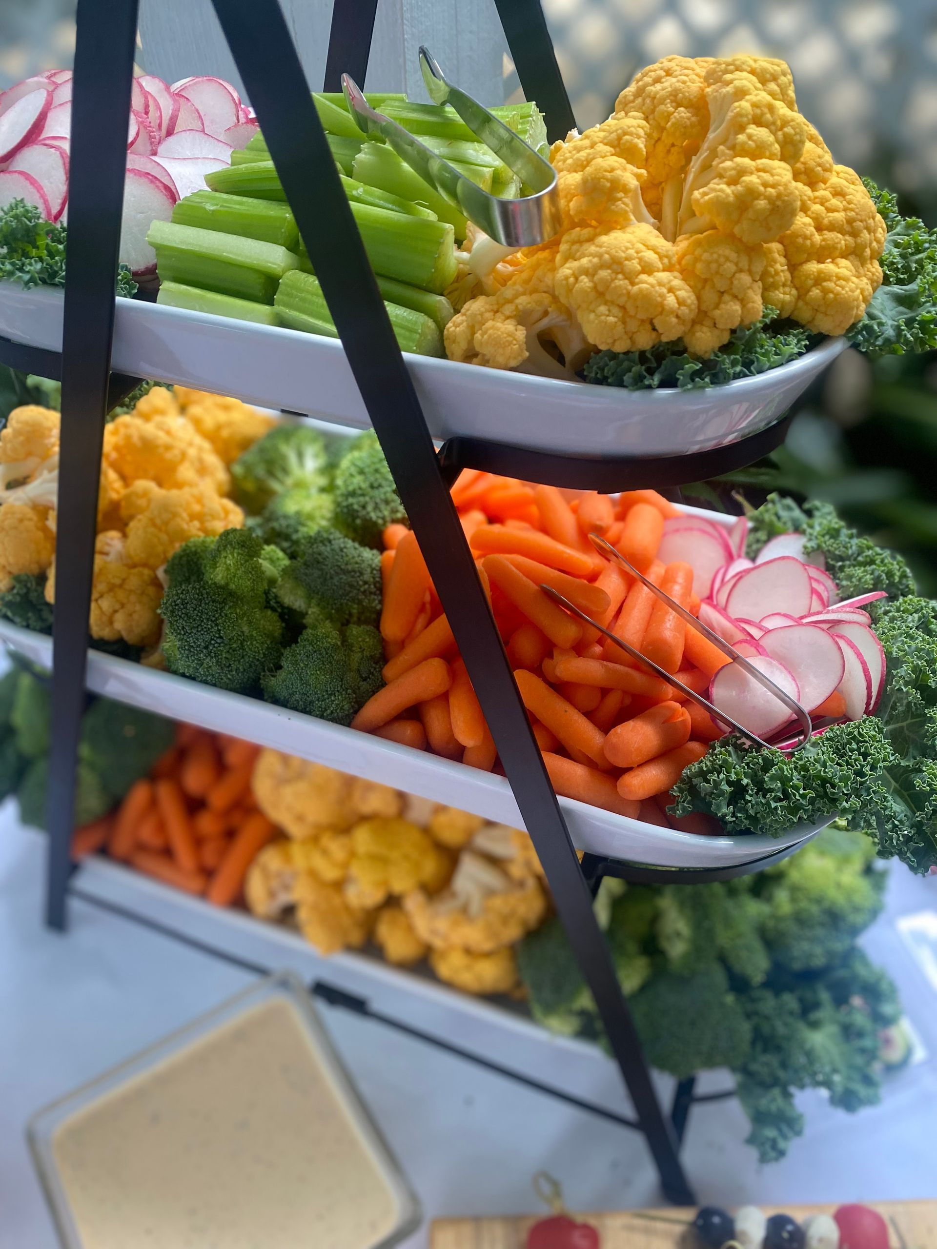 Tiered vegetable platter with radishes, celery, cauliflower, carrots, and broccoli.