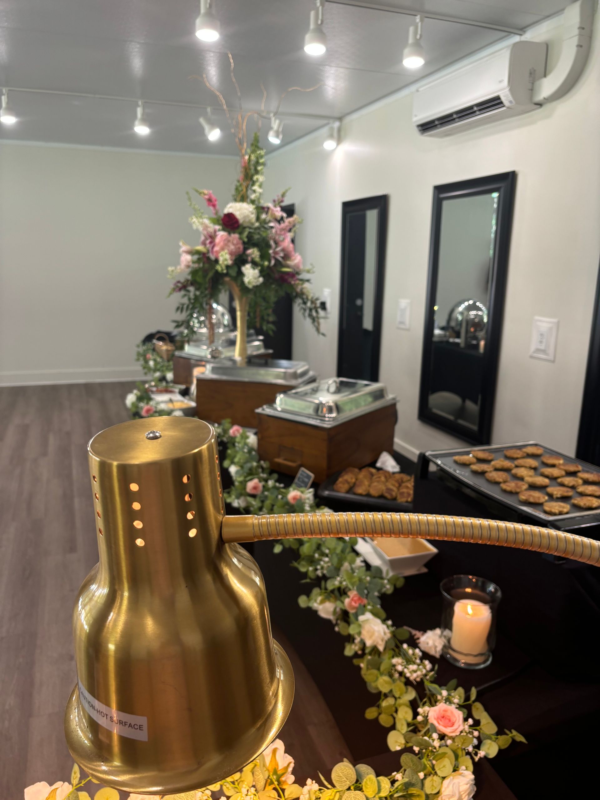 A buffet setup with a large floral arrangement and food warmers in a bright, white room.