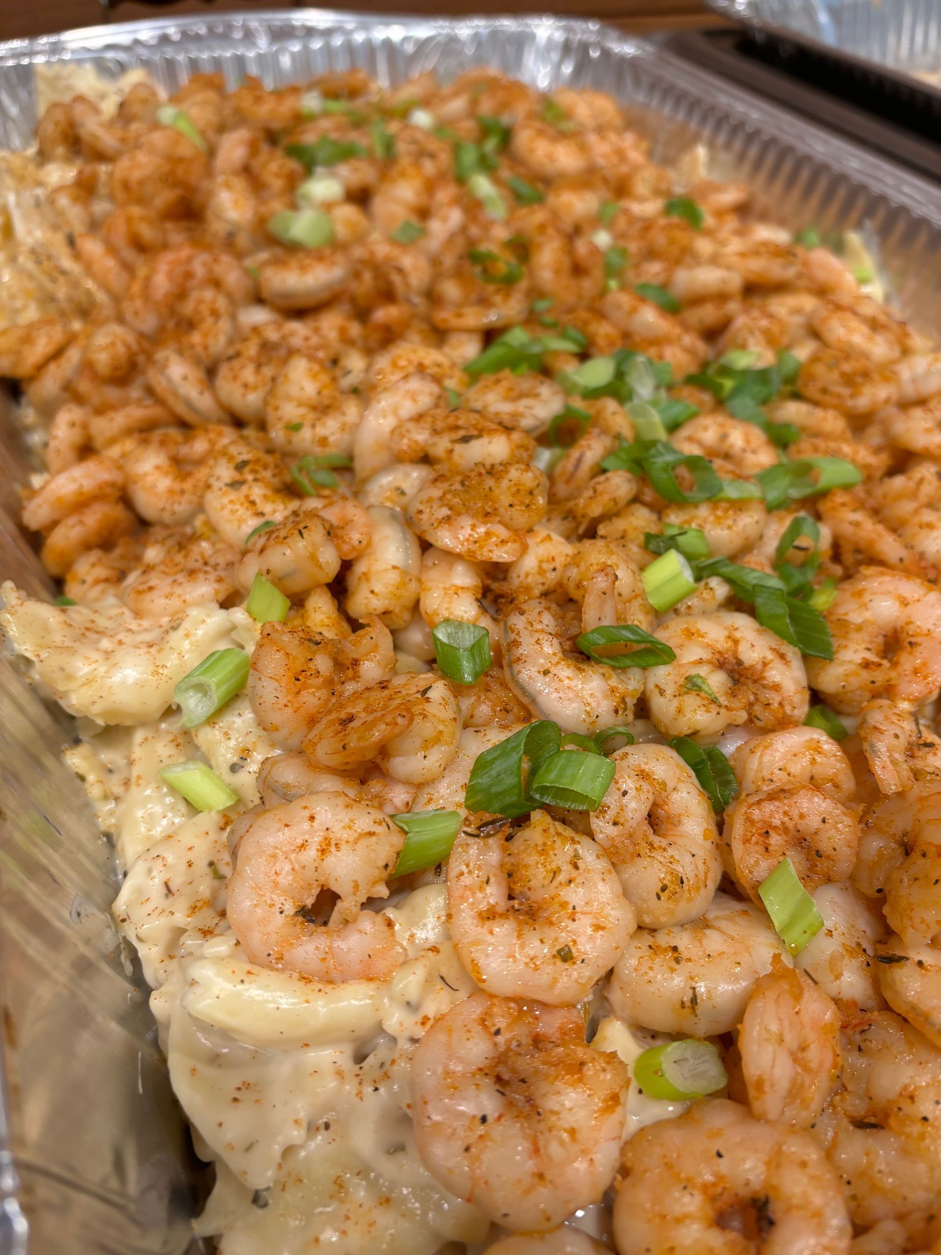 Tray of creamy pasta dish topped with seasoned shrimp and chopped green onions.