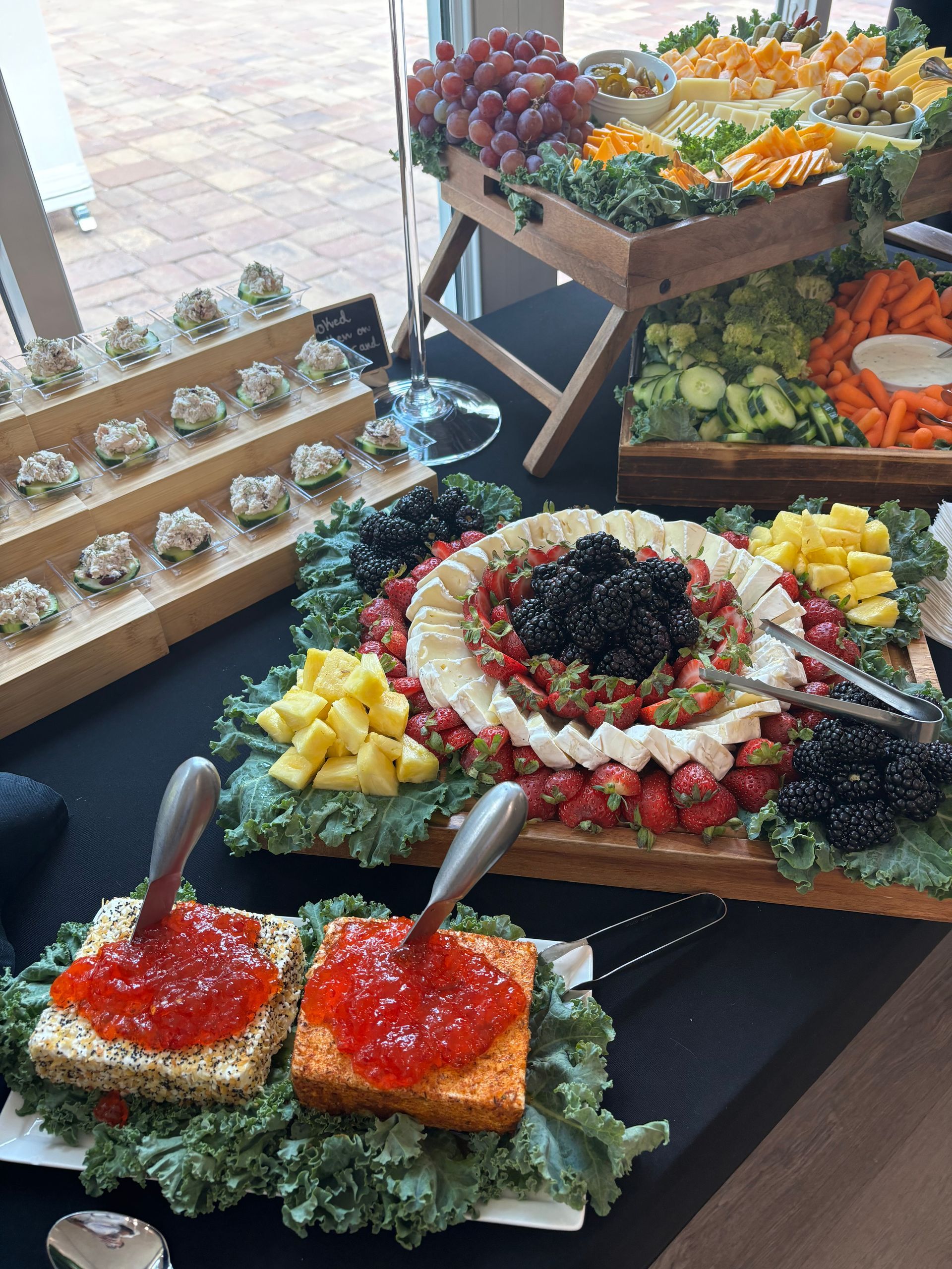 A buffet spread with various foods: cheese, fruit, vegetables, and appetizers, displayed on wooden platters and tiered stands.