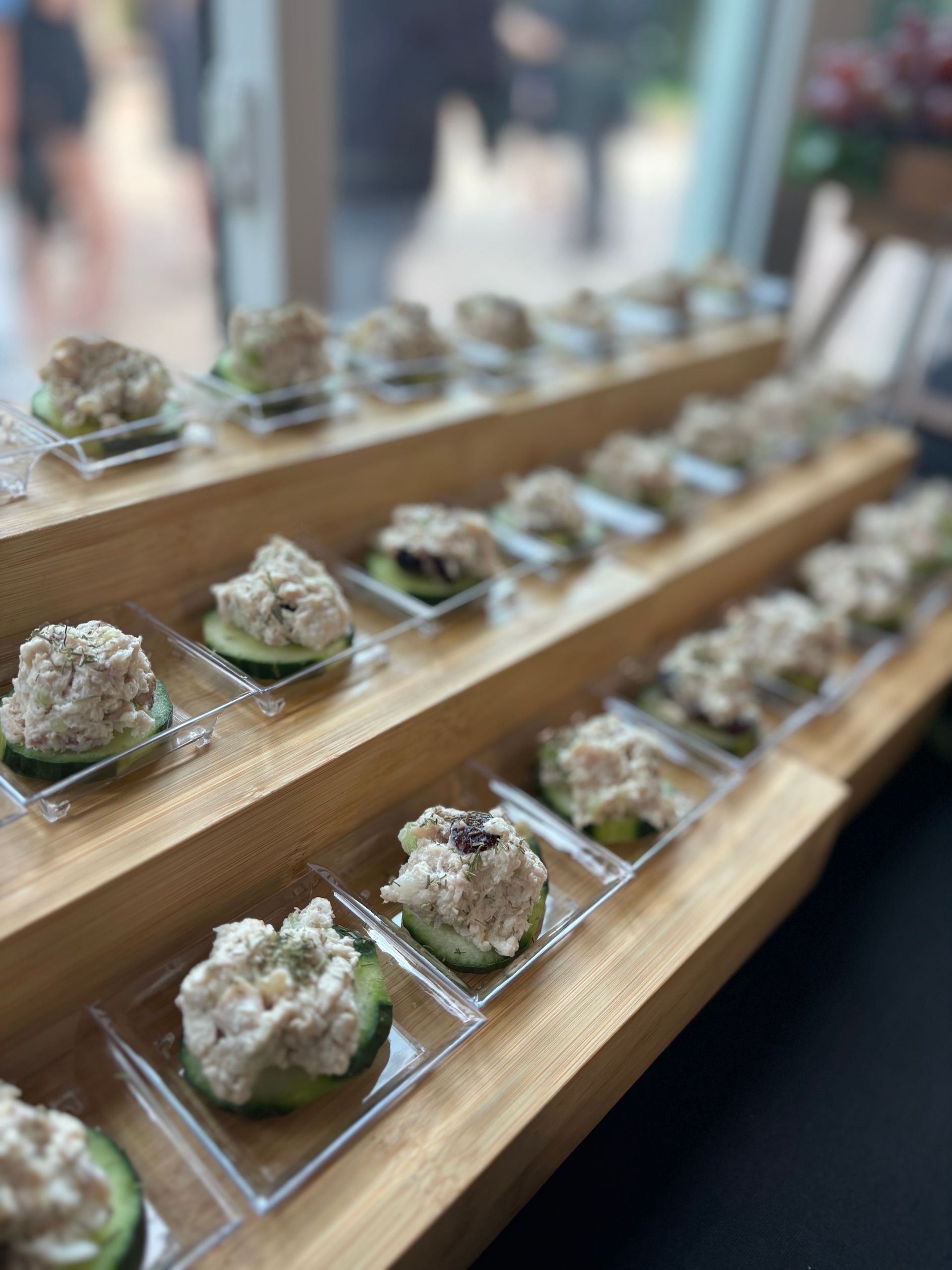 Appetizers, tuna salad on cucumber slices, arranged on tiered wooden serving boards.