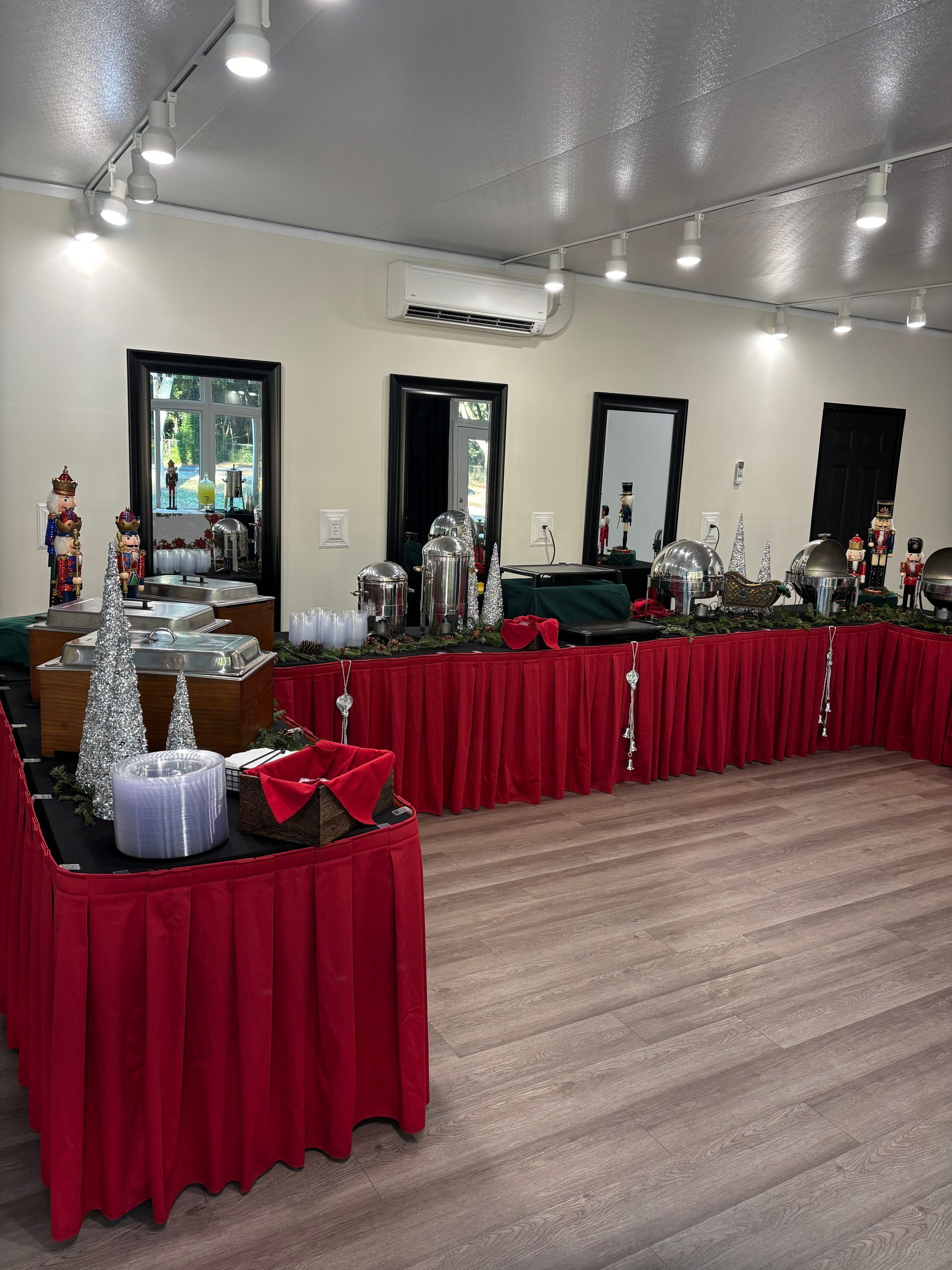 Buffet tables draped in red, set for a holiday event. Serving dishes are filled with food, with a decorative holiday theme.