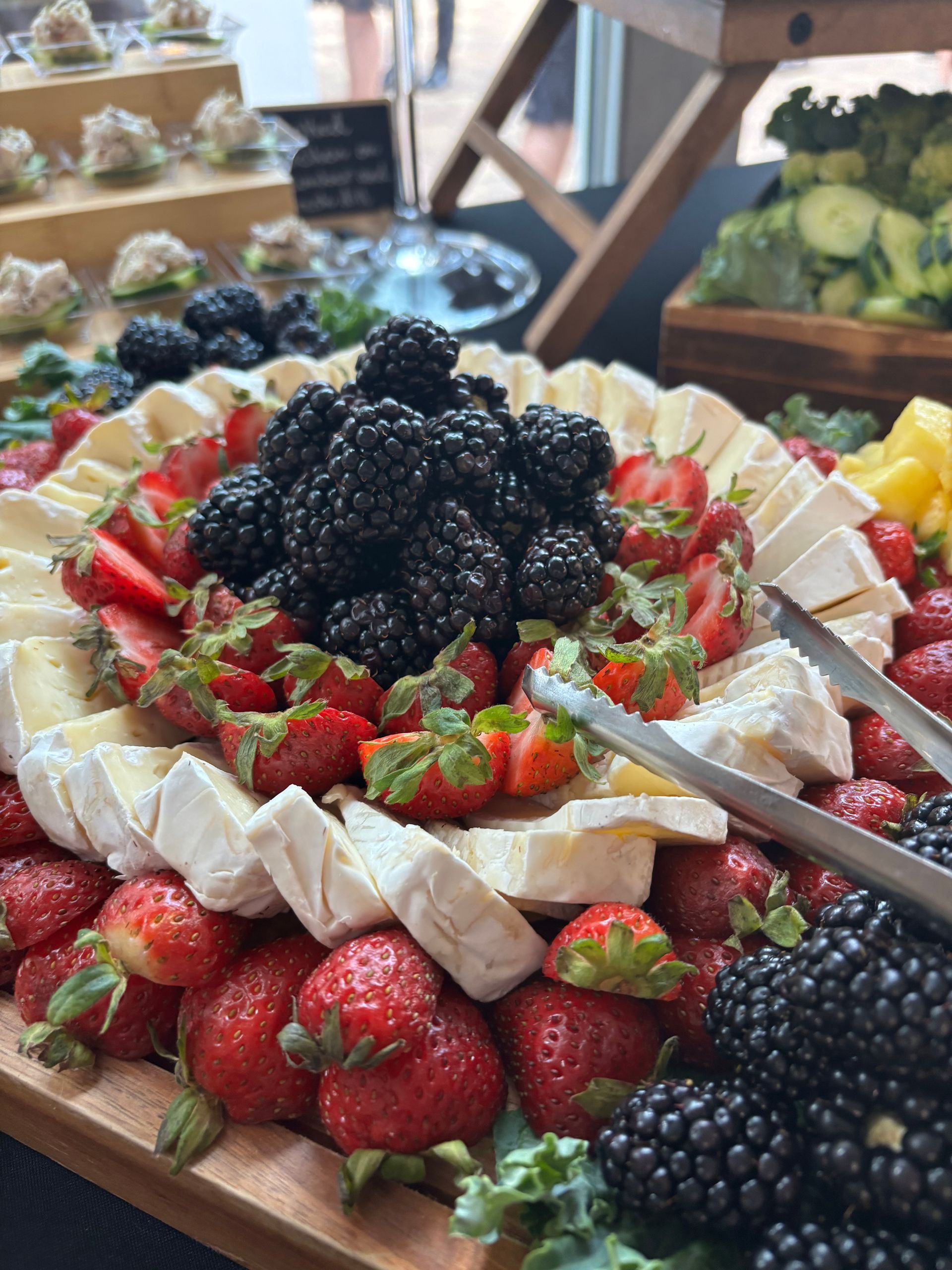 A colorful fruit and cheese platter. Strawberries, blackberries, and brie cheese arranged around a wooden board.