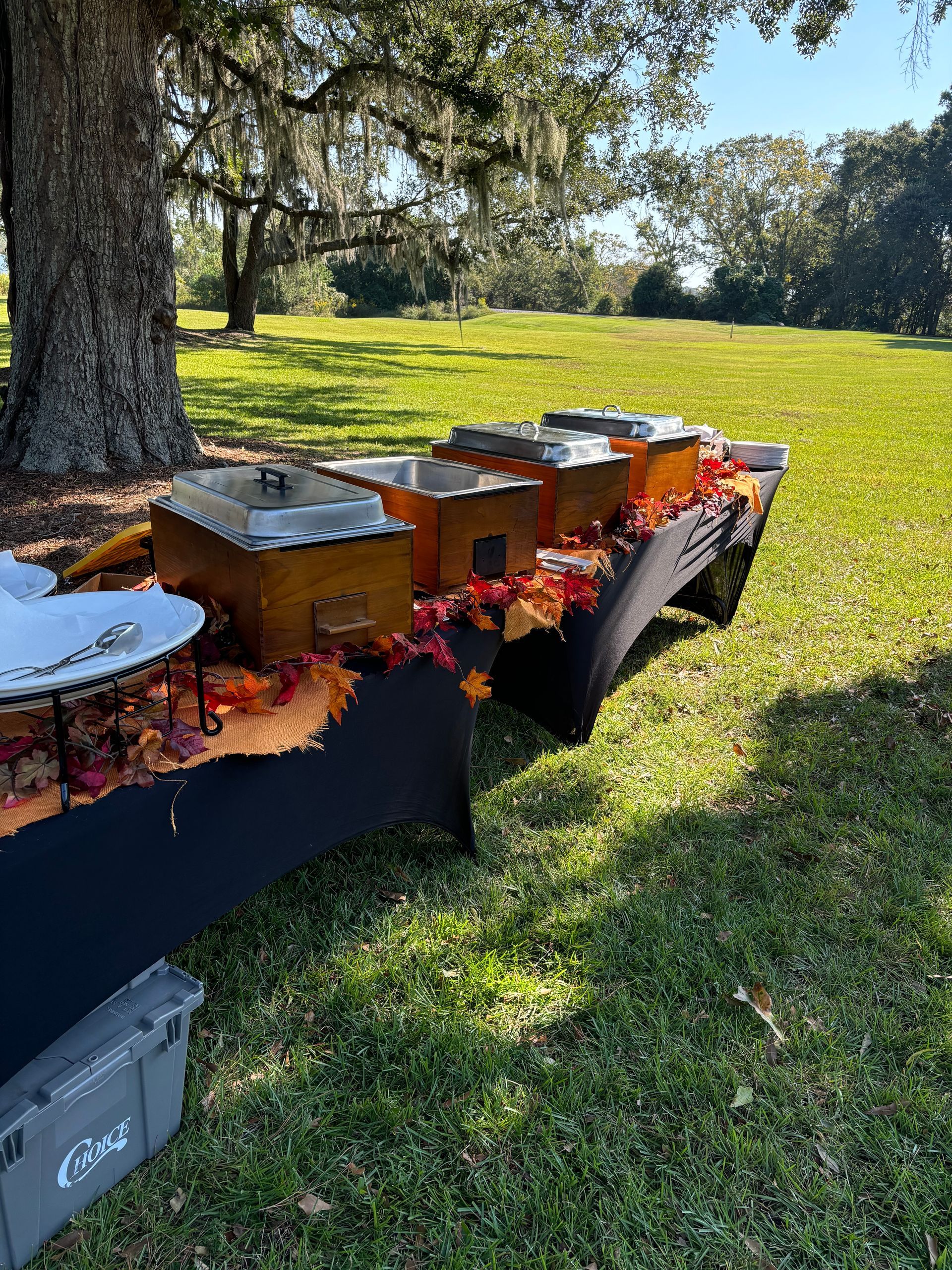 Buffet table with chafing dishes set up outdoors on a sunny day. Fall leaves and decorations on the table.