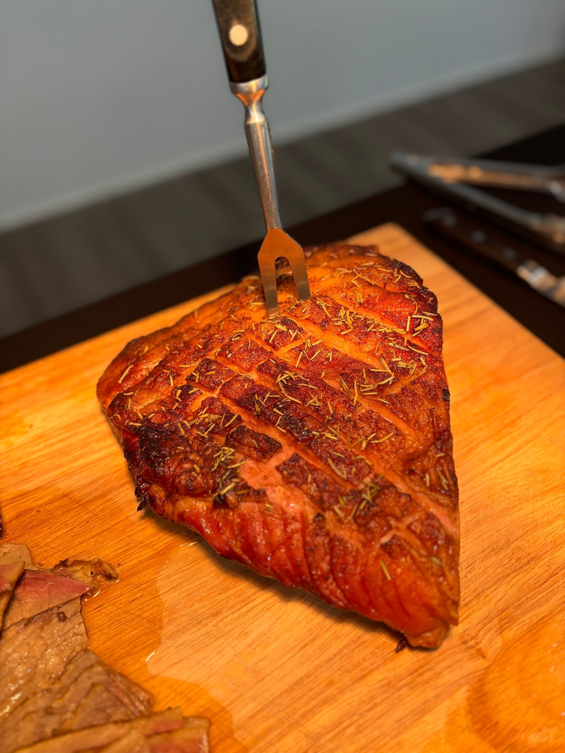 A roasted piece of meat with a fork in it, resting on a wooden cutting board.