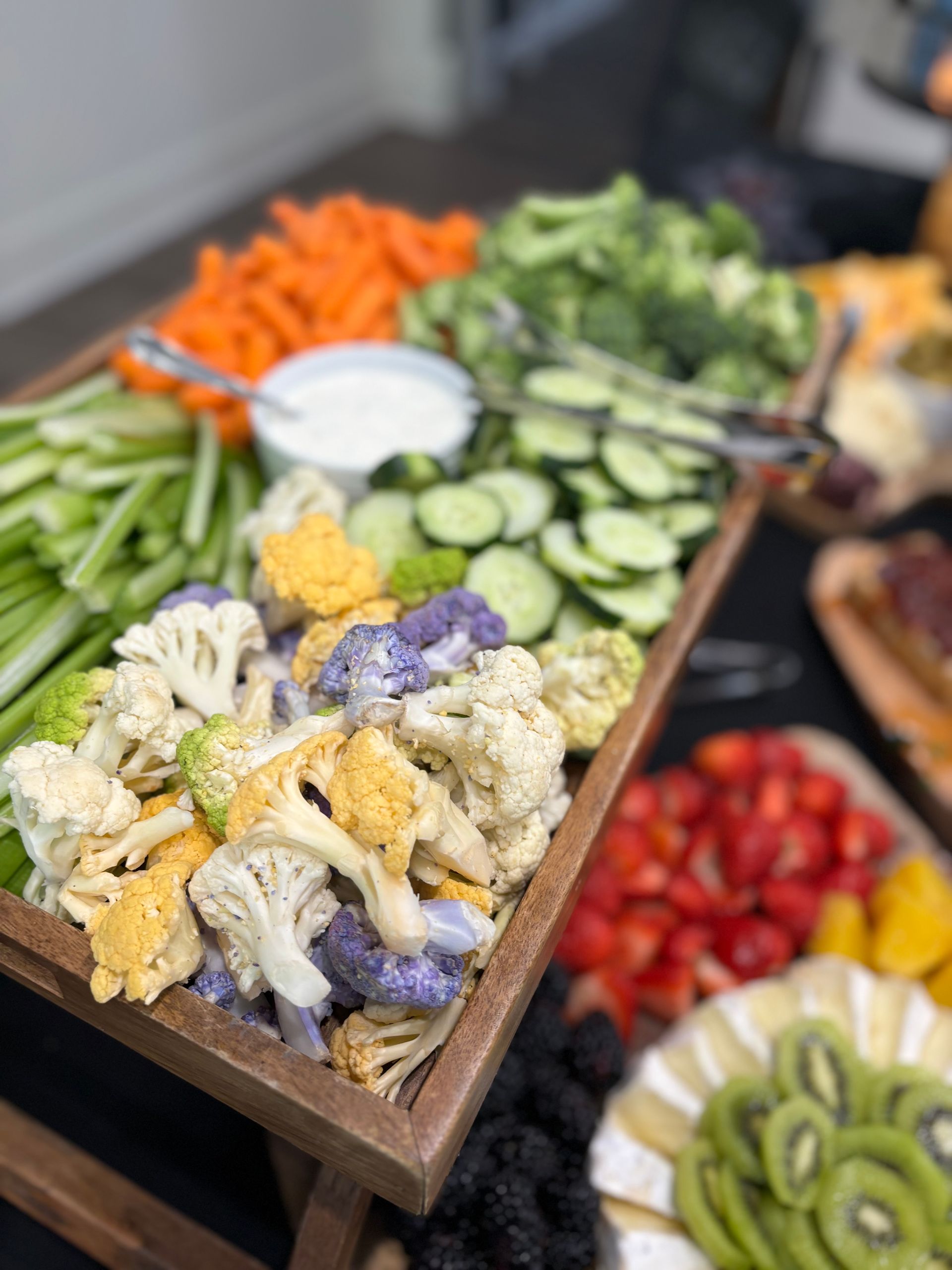 Vegetable platter with colorful cauliflower, carrots, celery, cucumbers, broccoli, and dip. Served on a wooden tray.