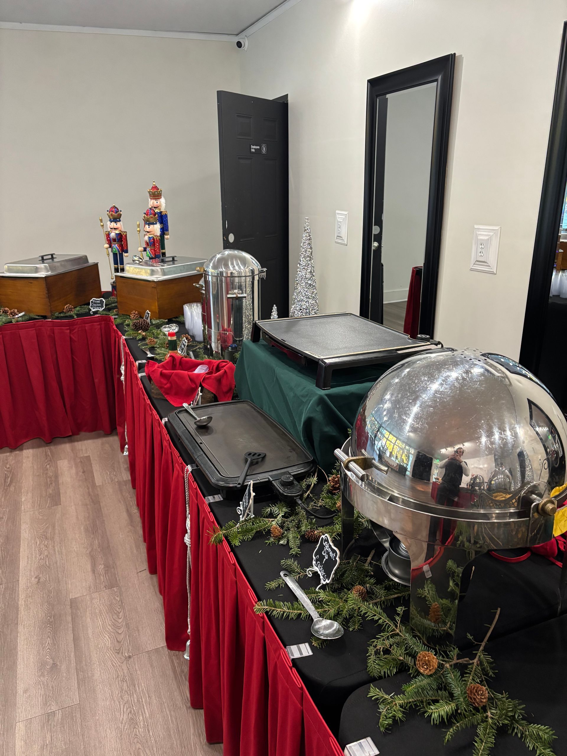 A buffet table set for a festive event with red skirting, various food warmers, and holiday decorations.