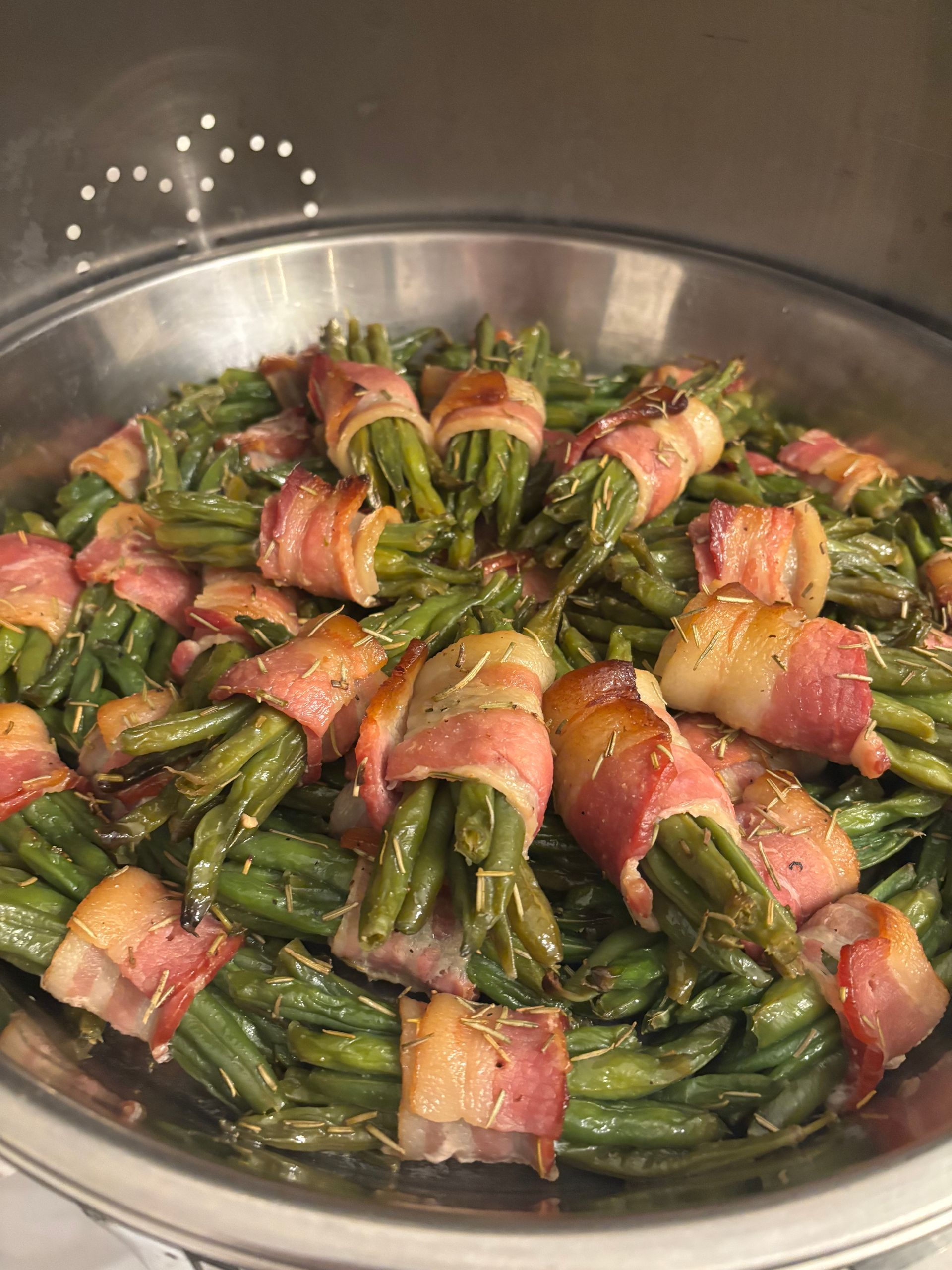 Green beans wrapped in bacon, cooked in a large metal bowl. The beans are bright green with brown, crispy bacon.