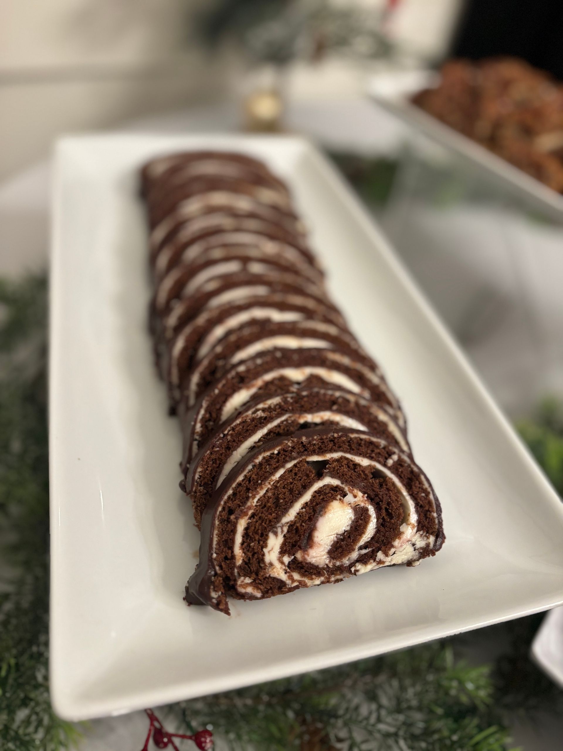 Sliced chocolate cake roll with cream filling on a white platter, decorated for the holidays.