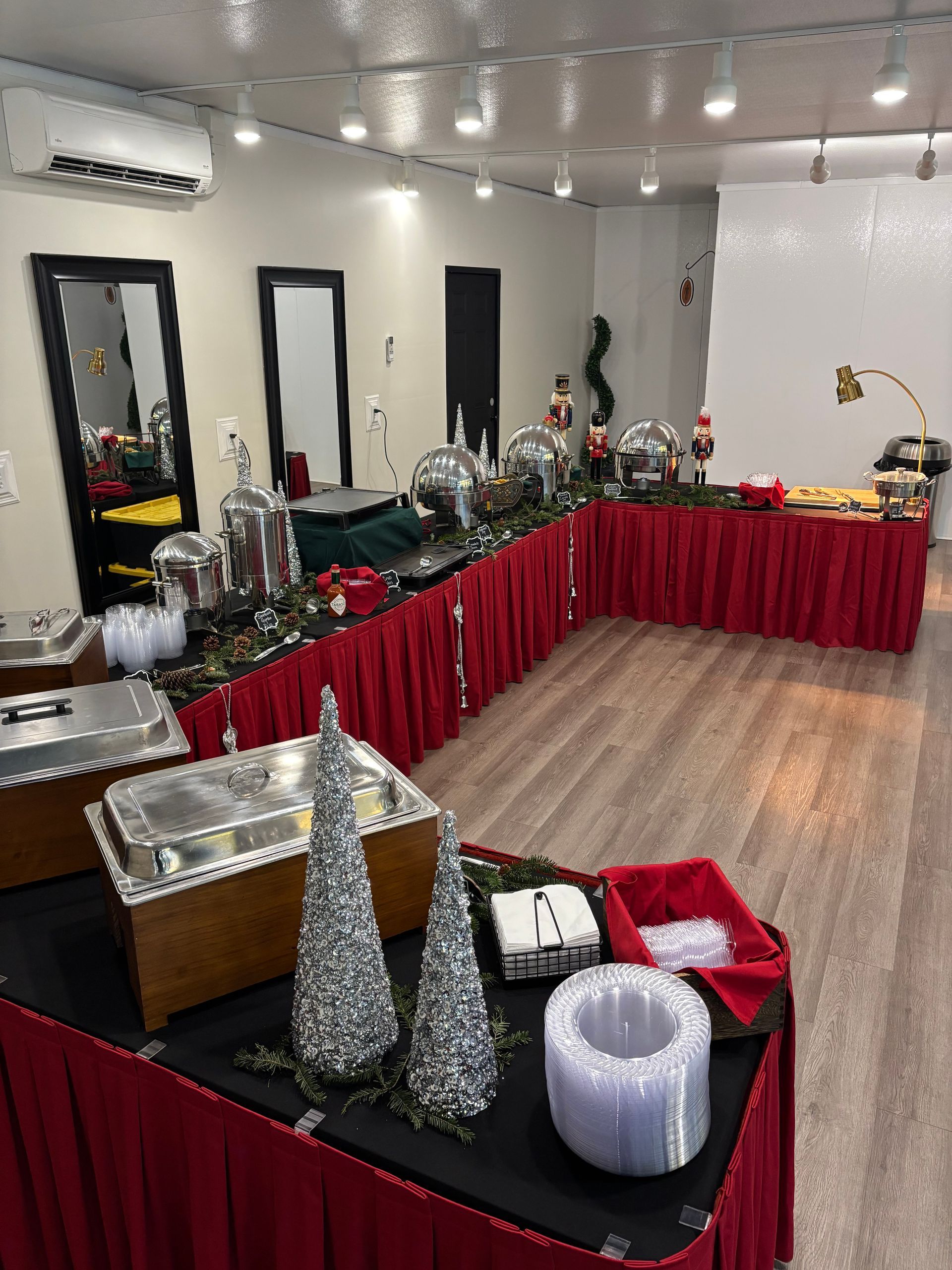 A buffet with red tablecloths, silver serving dishes, and Christmas decorations in a brightly lit room with wood flooring.