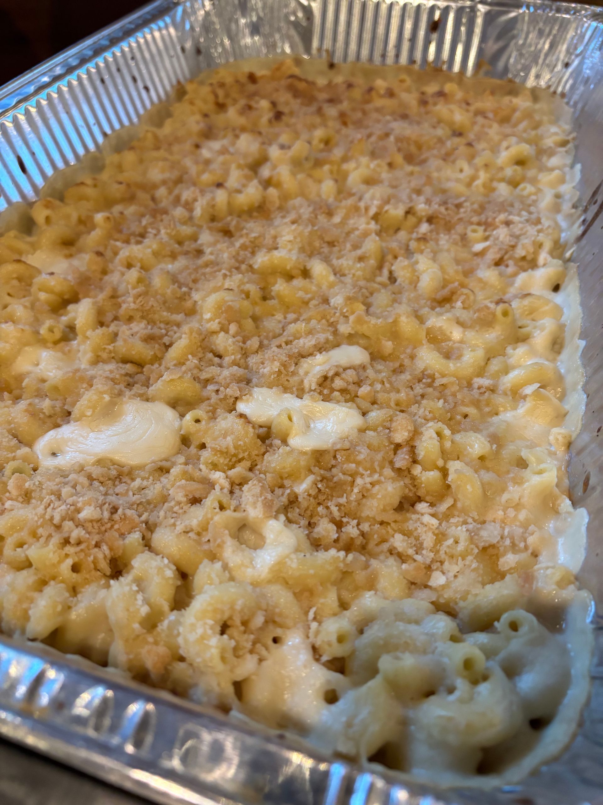 Baked mac and cheese in a foil pan; golden-brown, with a breadcrumb topping.