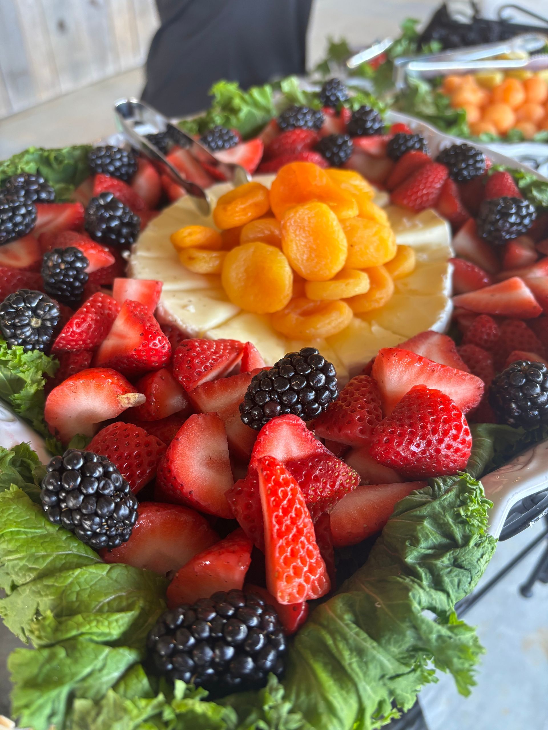 Fruit platter with strawberries, blackberries, and dried apricots around a brie cheese wheel.