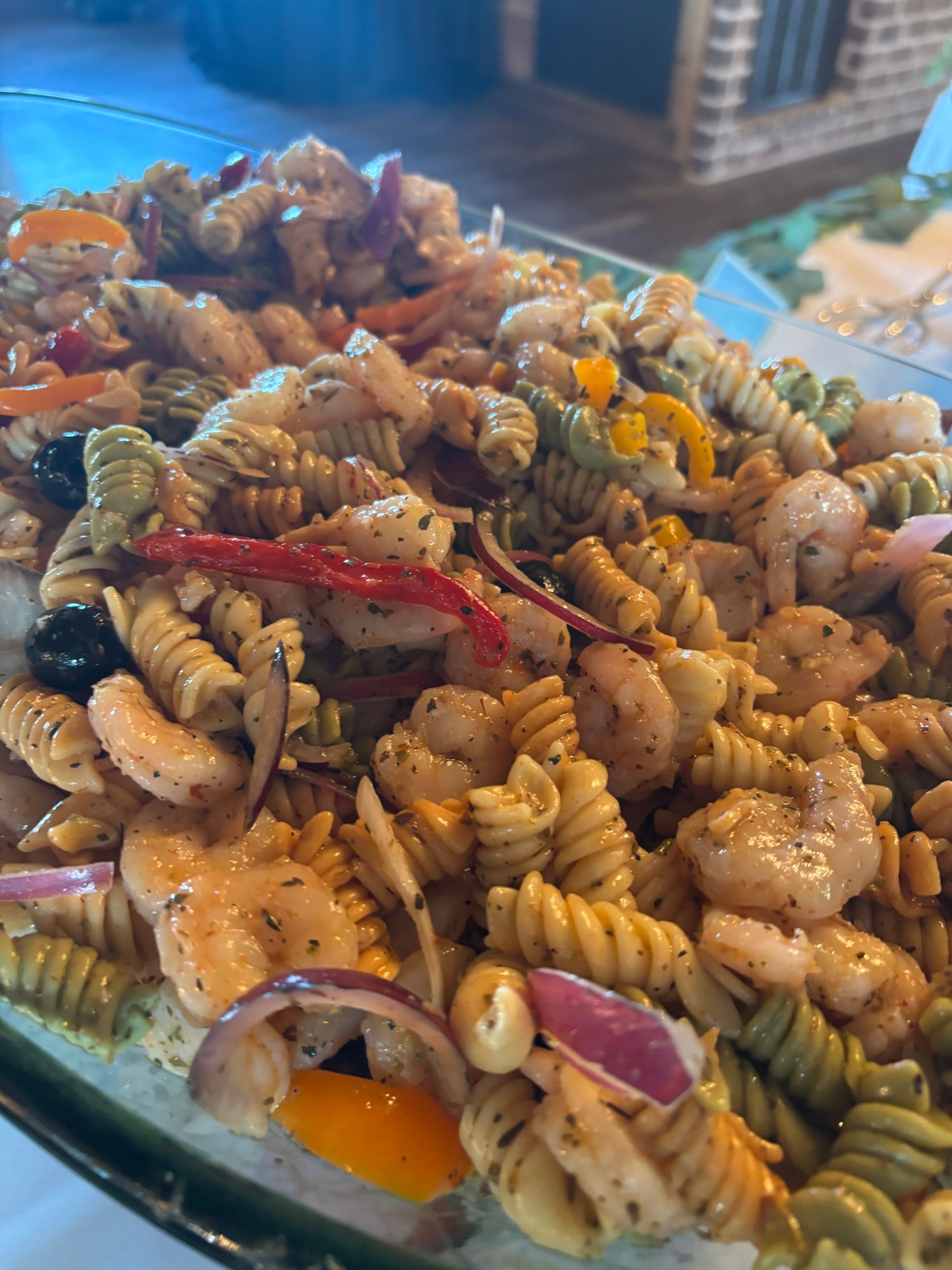 Pasta salad with shrimp, red onion, olives, and bell peppers in a serving dish.