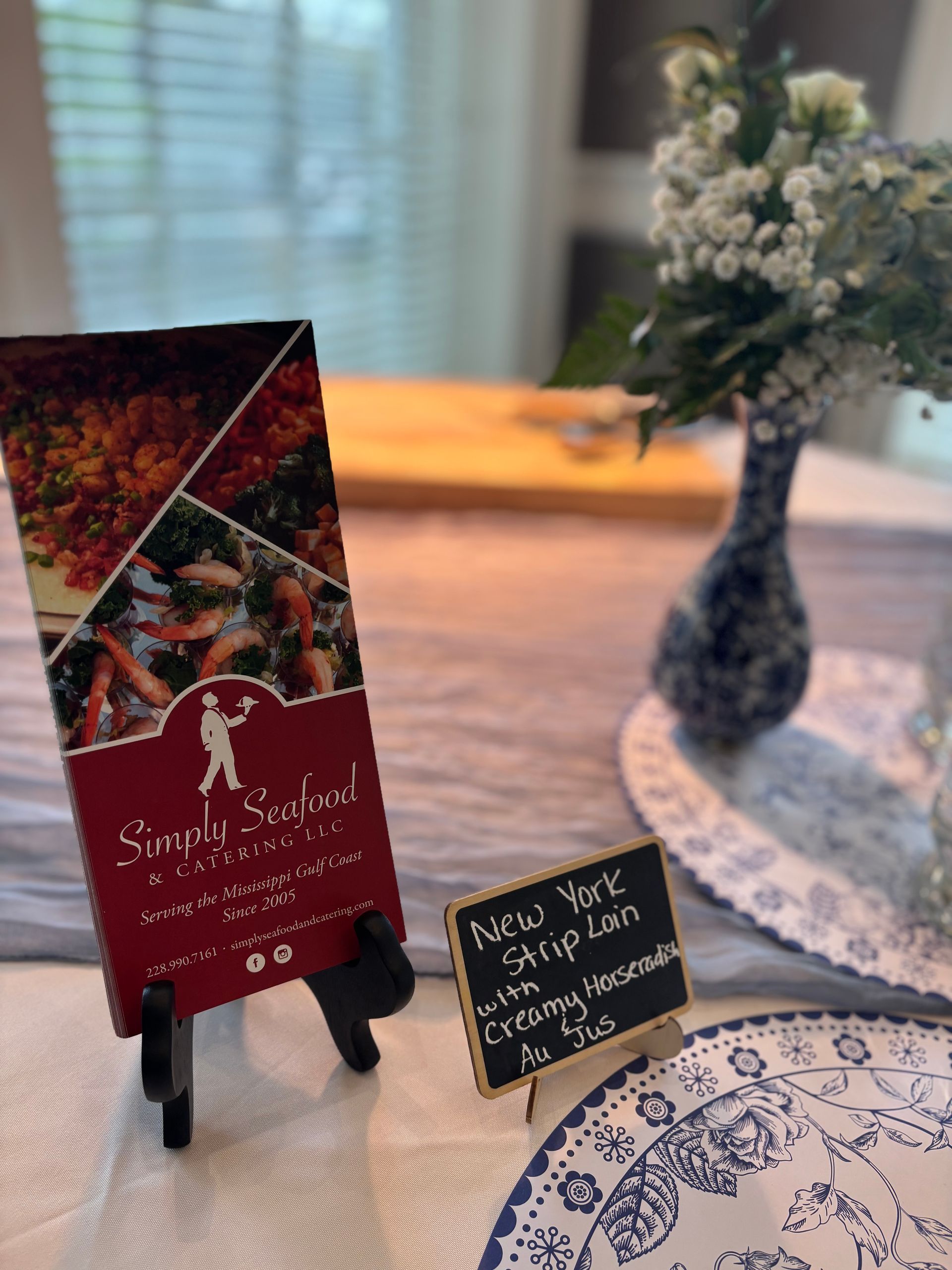 A restaurant menu and chalkboard sign on a table set for a meal. Menu is dark red and has food photos. The sign advertises a New York strip loin for $50.