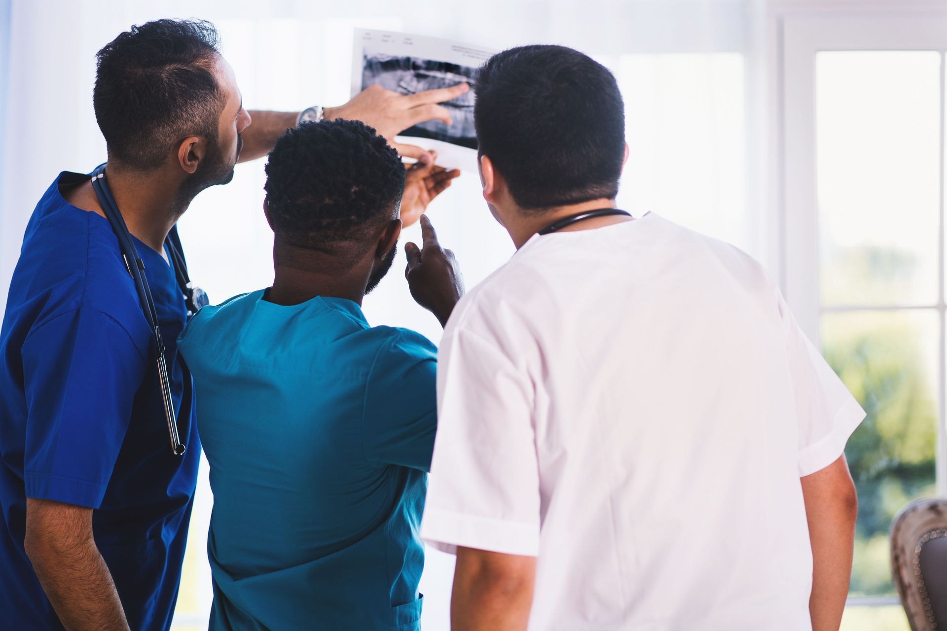 Three people in scrubs and a white coat reviewing a wall-mounted medical image in a clinic.
