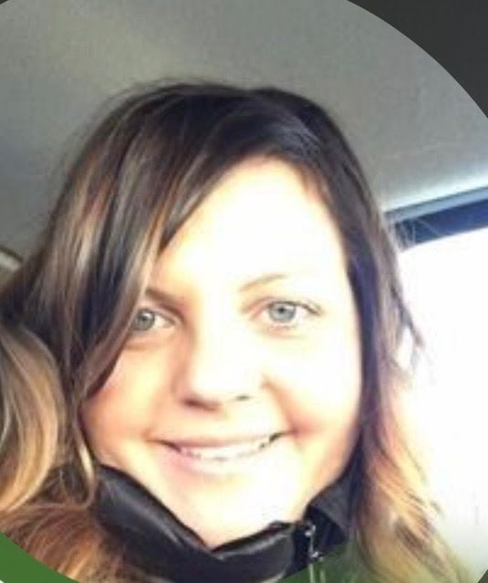 Woman with brown hair smiling, wearing a dark jacket, natural light.