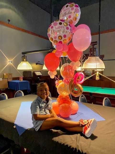 A happy 6 year old sitting on a table with a large helium balloon centerpiece behind her.