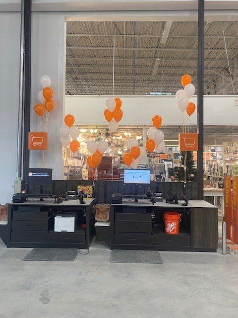 The cashier station at a Home Depot store with lots of orange and white helium balloons floating around it.