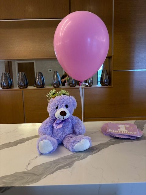 A purple teddy bear sitting on a dinner table as a centerpiece.