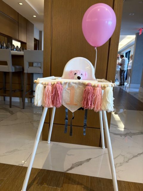 a photo of a white high chair with a multiple colored pink garland with a 1 in the middle and yarn tassels on either side.